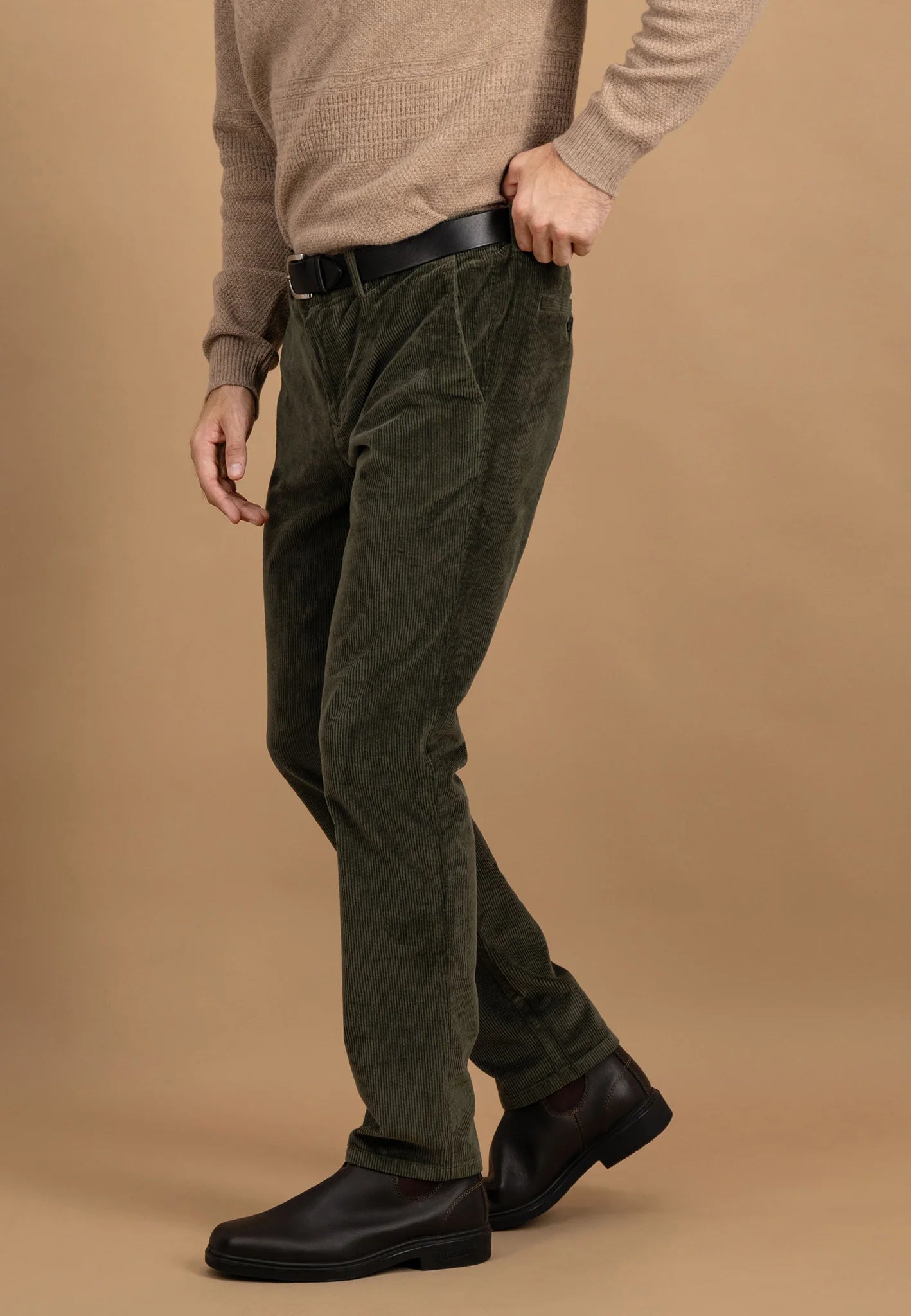 Person wearing olive green corduroy pants and a beige sweater on a brown background