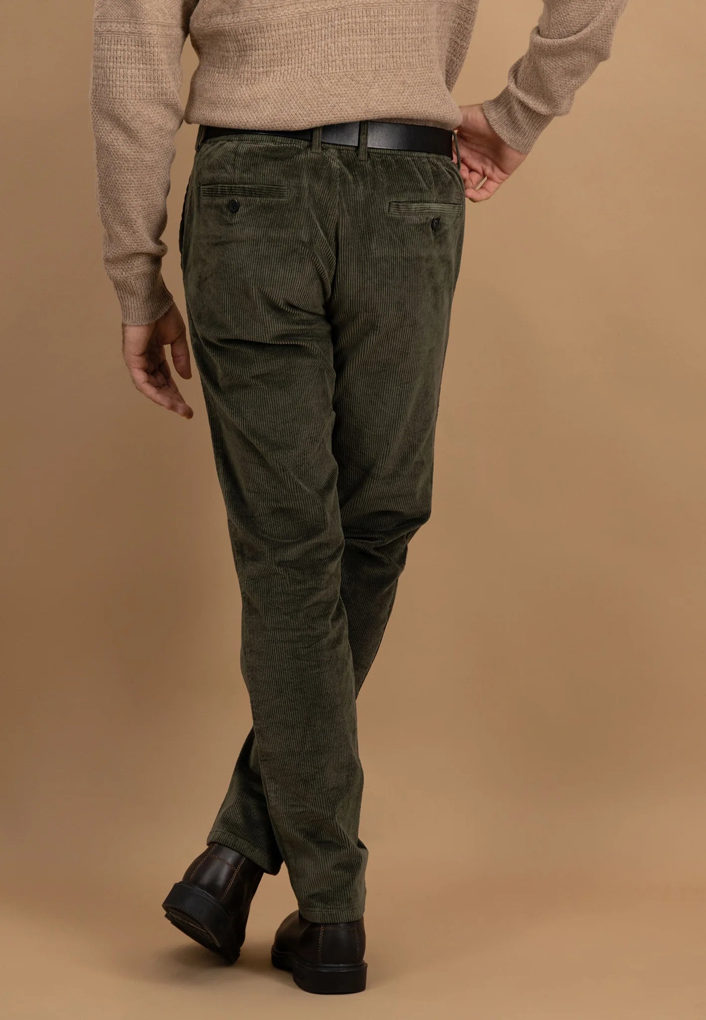 Person wearing olive green pants and a beige sweater on a brown background