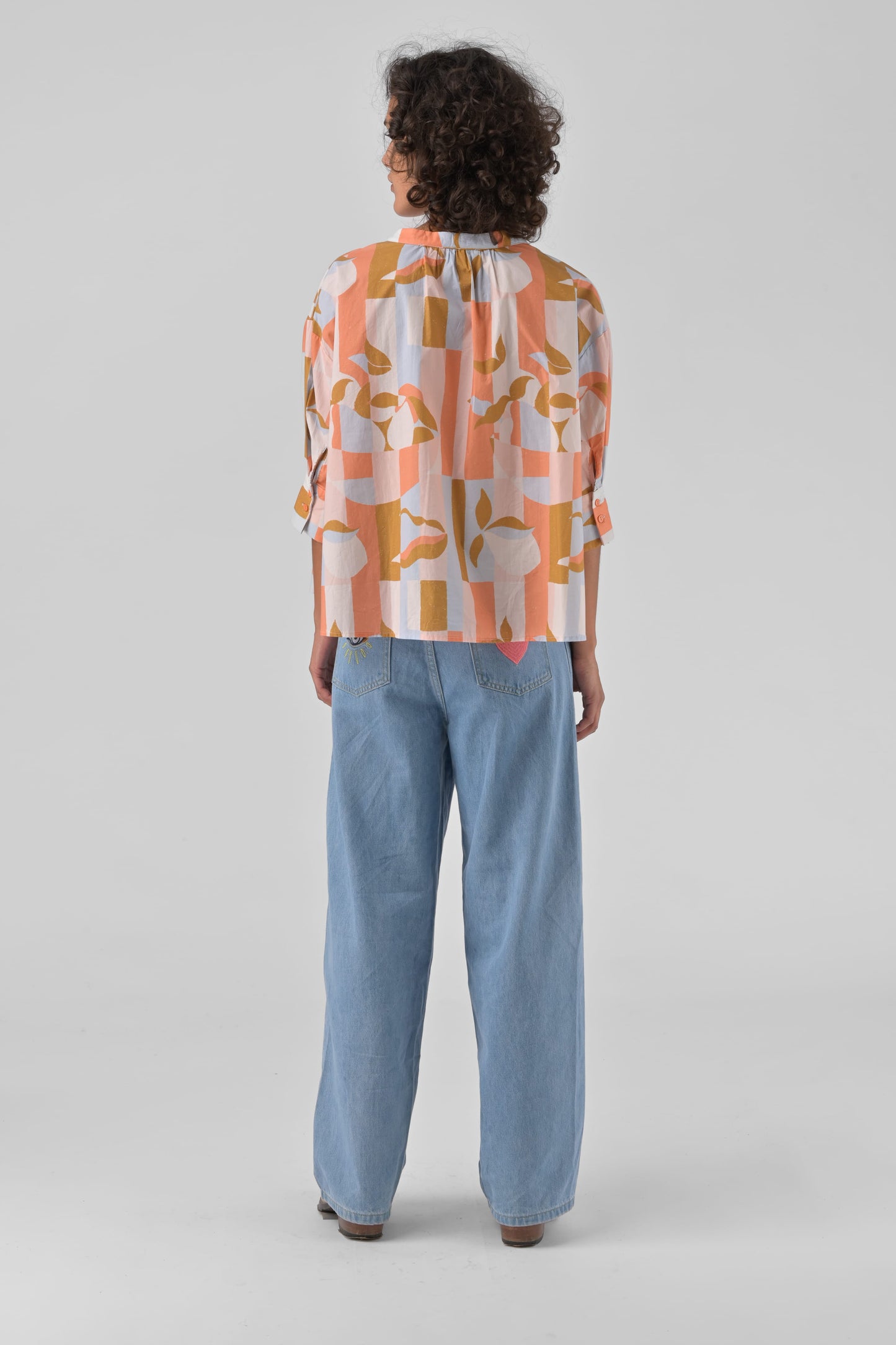 Person wearing a patterned shirt and blue pants on a light gray background