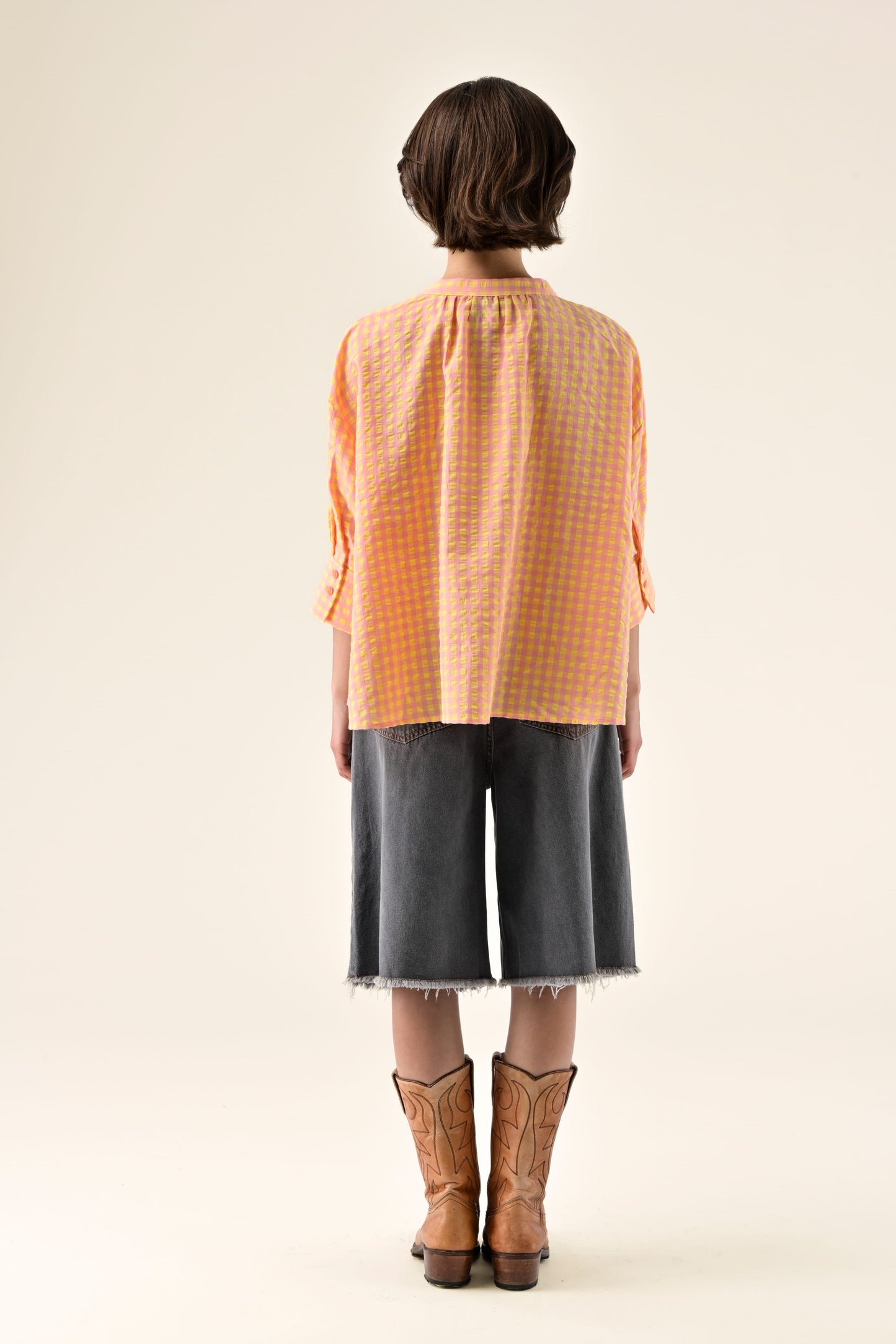 Person wearing an orange checkered shirt, black pants, and brown boots on a white background