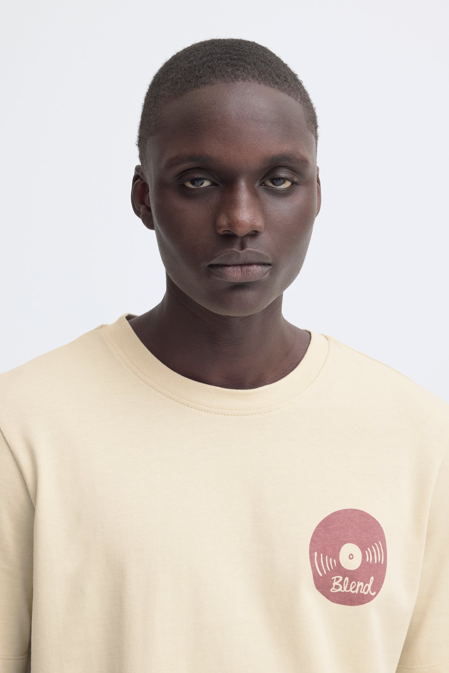 Man wearing a beige t-shirt with a logo on a white background