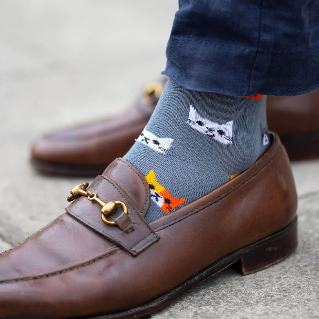 Gray socks with cat designs worn with brown loafers on a neutral background