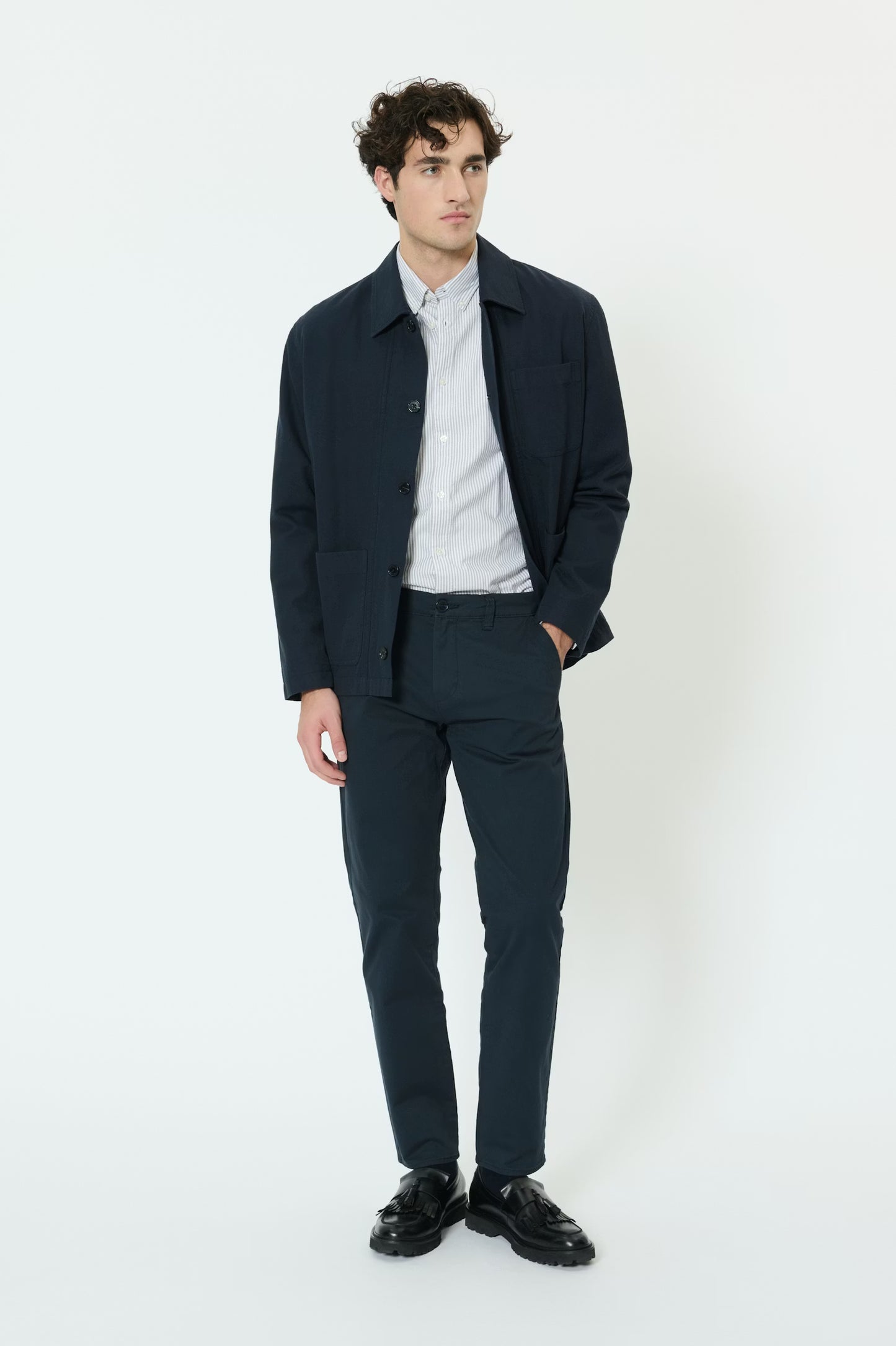 Man wearing a navy jacket, light shirt, and dark pants on a white background