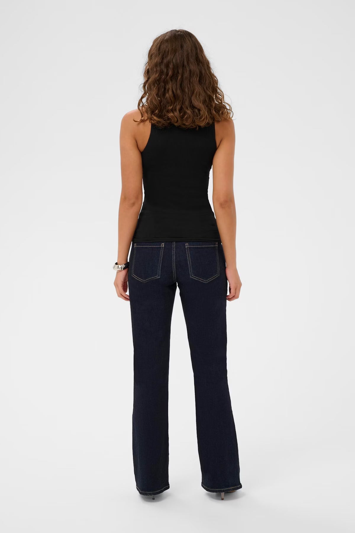Person wearing a black sleeveless top and dark blue jeans on a white background
