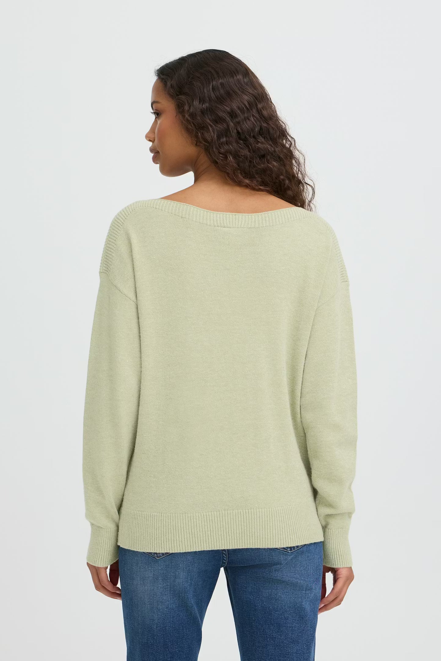 Woman wearing a light green sweater and blue jeans on a white background