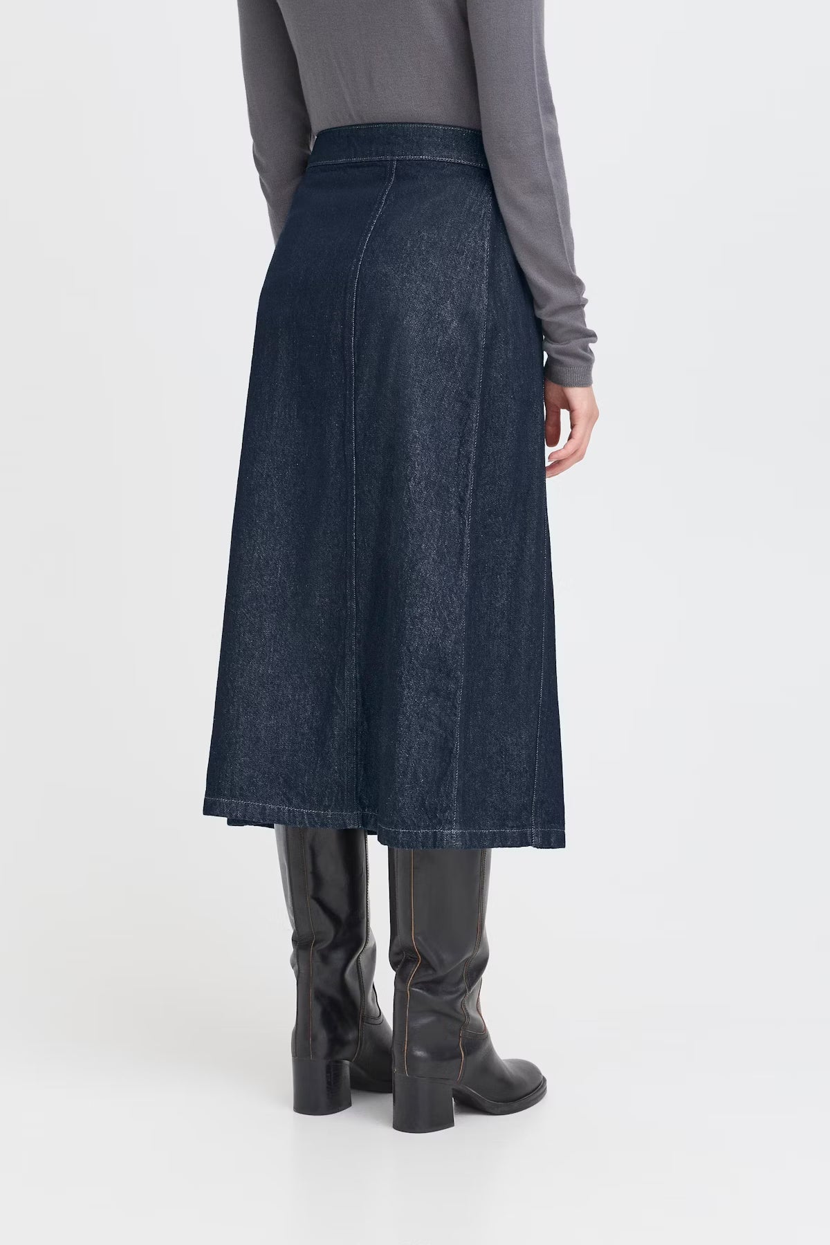 Person wearing a long dark denim skirt with a plain background