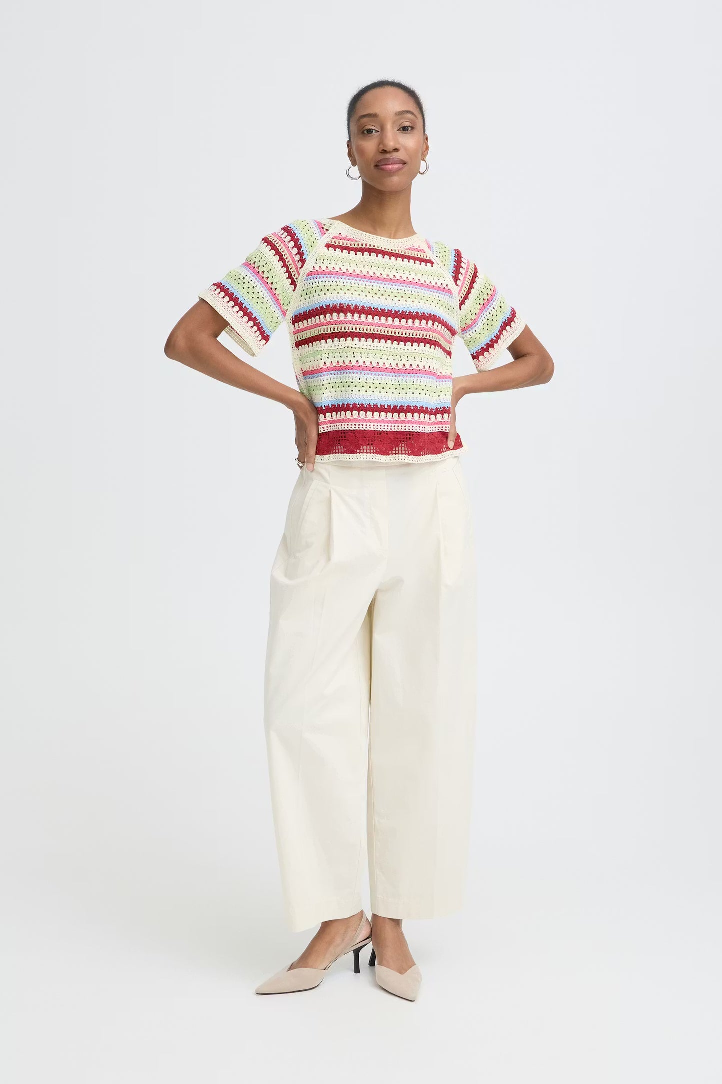 Woman wearing a striped sweater and white pants on a white background
