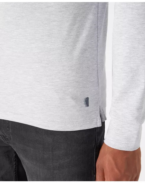 Close-up of a person wearing a white long-sleeve shirt with a small logo on a plain background