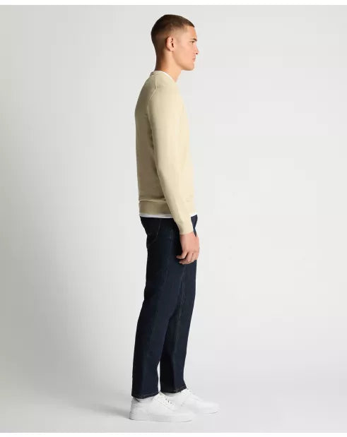 Man wearing a beige sweater and dark pants on a white background