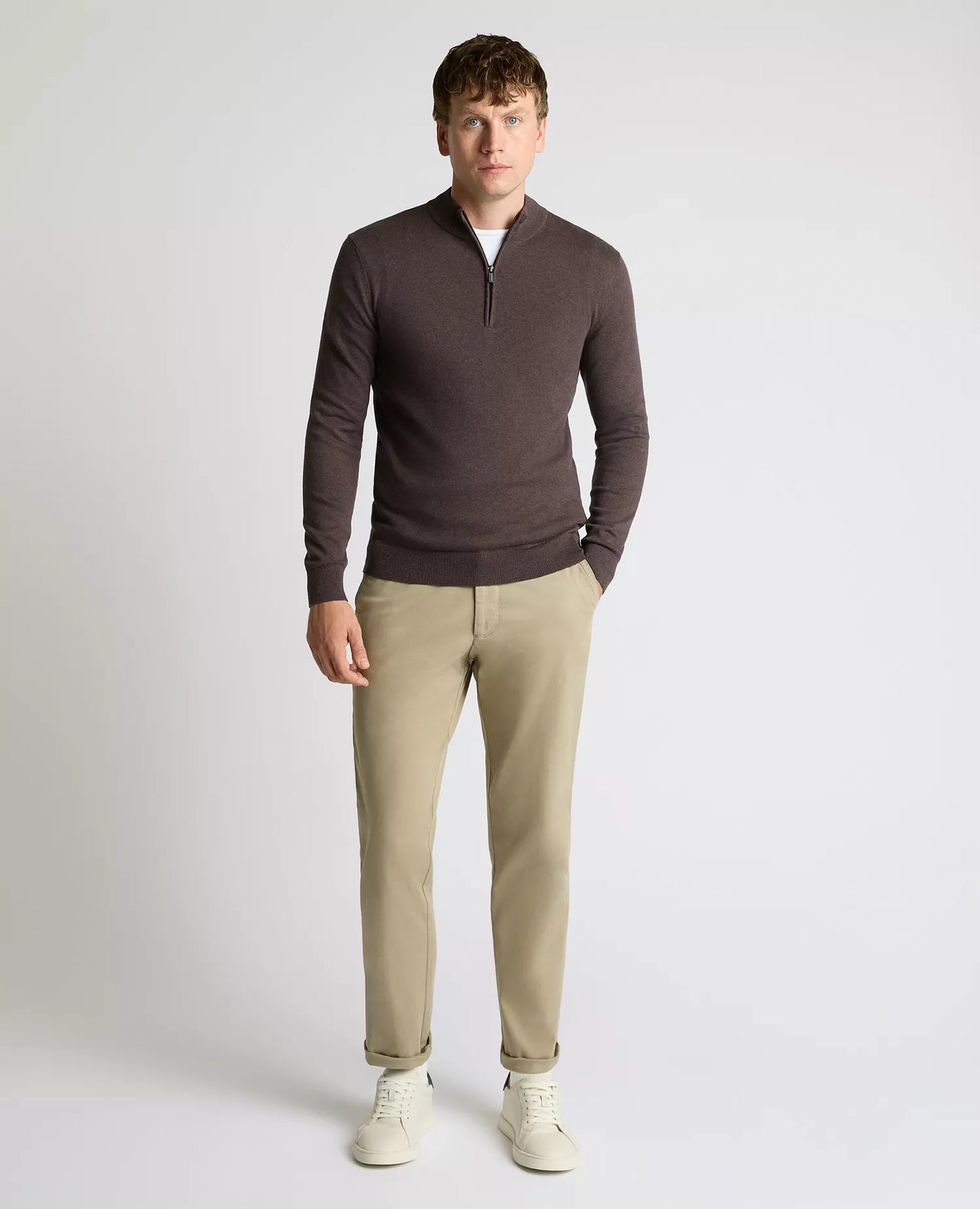 Man wearing a brown long-sleeve shirt and beige pants on a white background