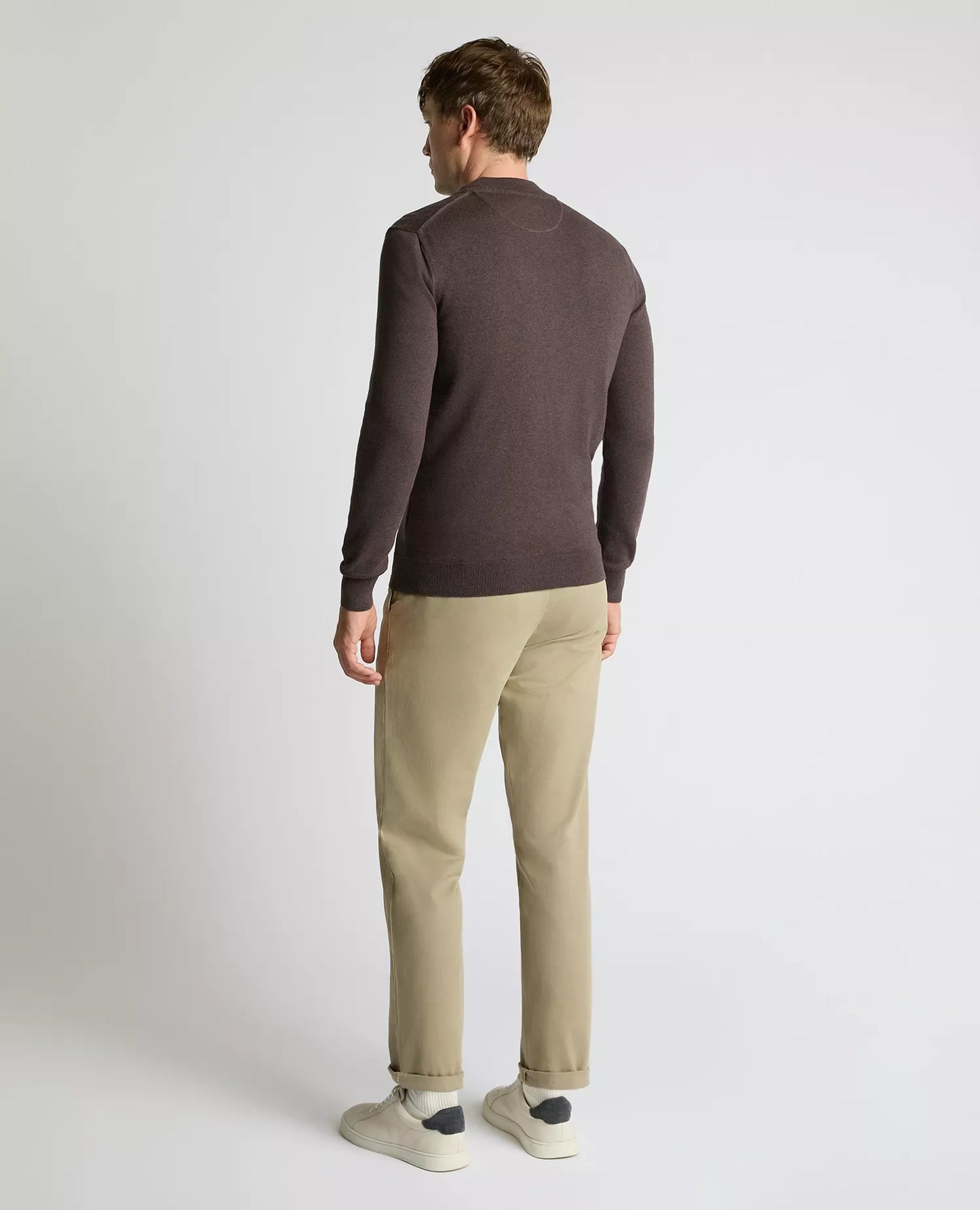 Man wearing a brown sweater and beige pants on a white background