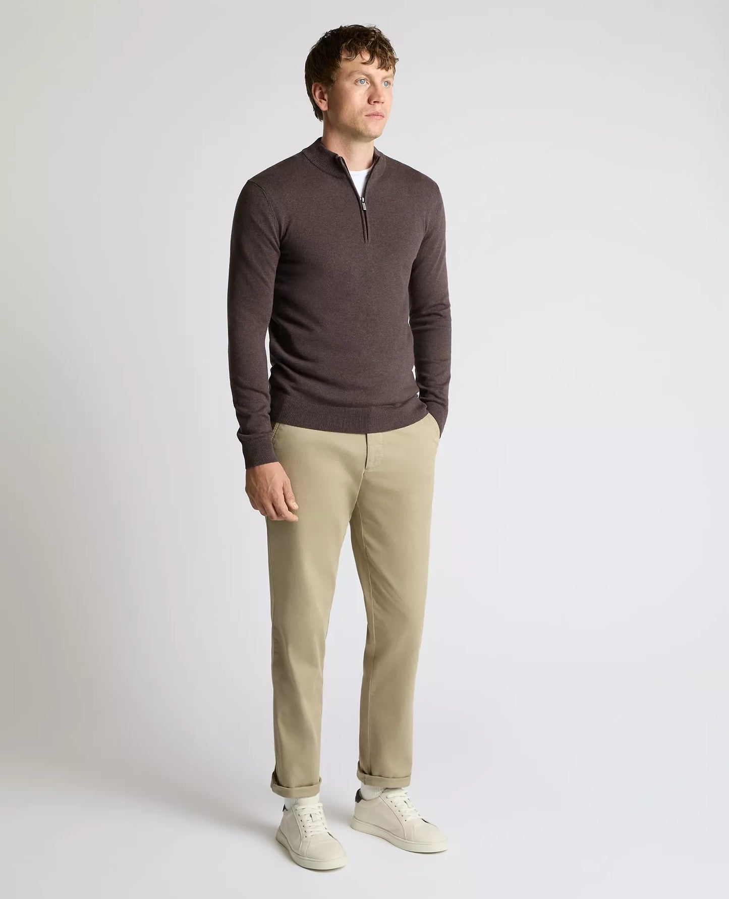 Man wearing a brown sweater and beige pants on a white background