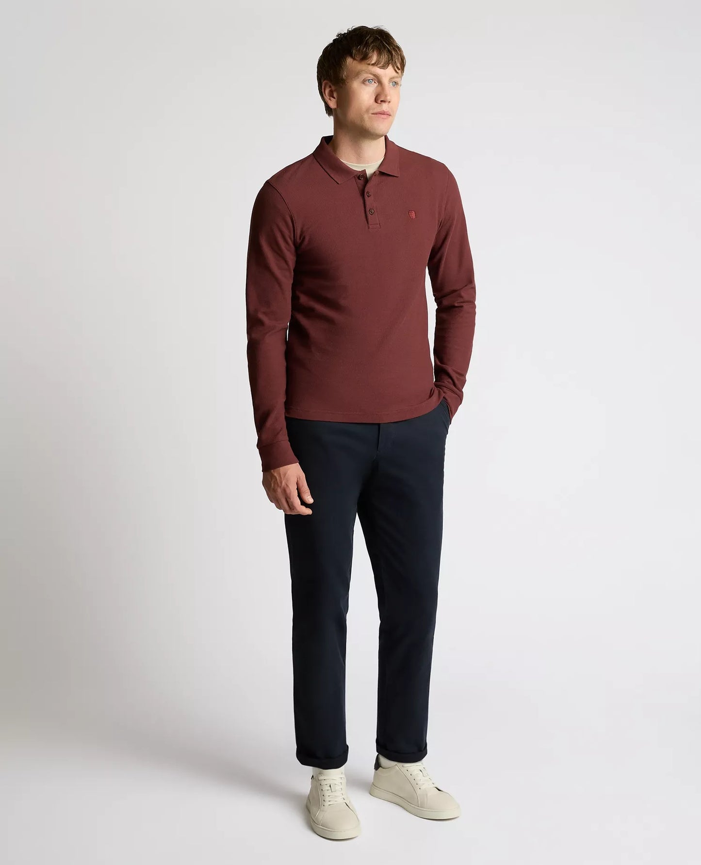 Man wearing a maroon long-sleeve polo shirt and dark pants on a white background