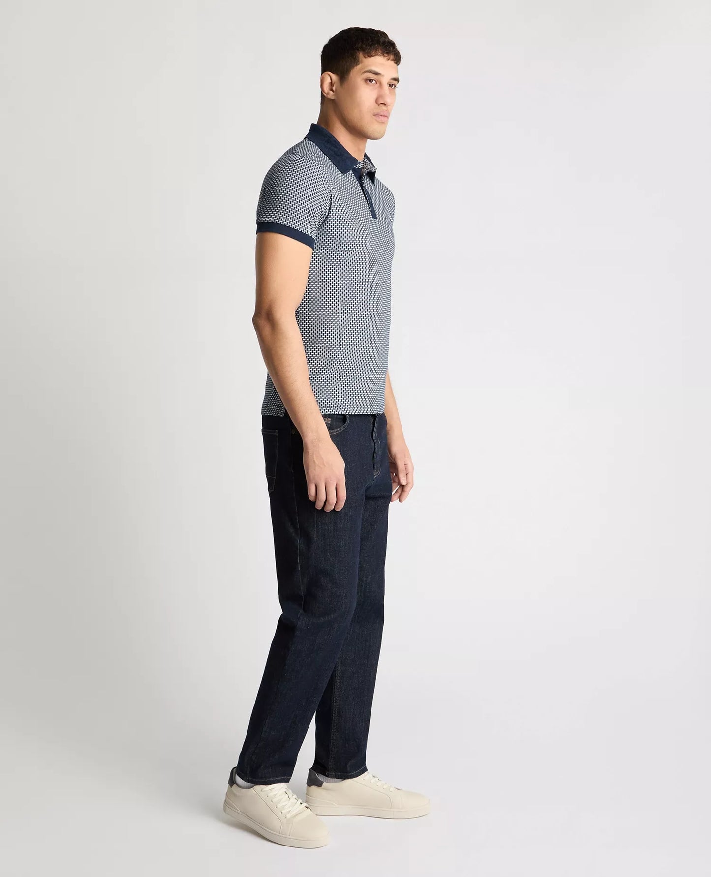 Man wearing a patterned polo shirt and dark pants on a light gray background