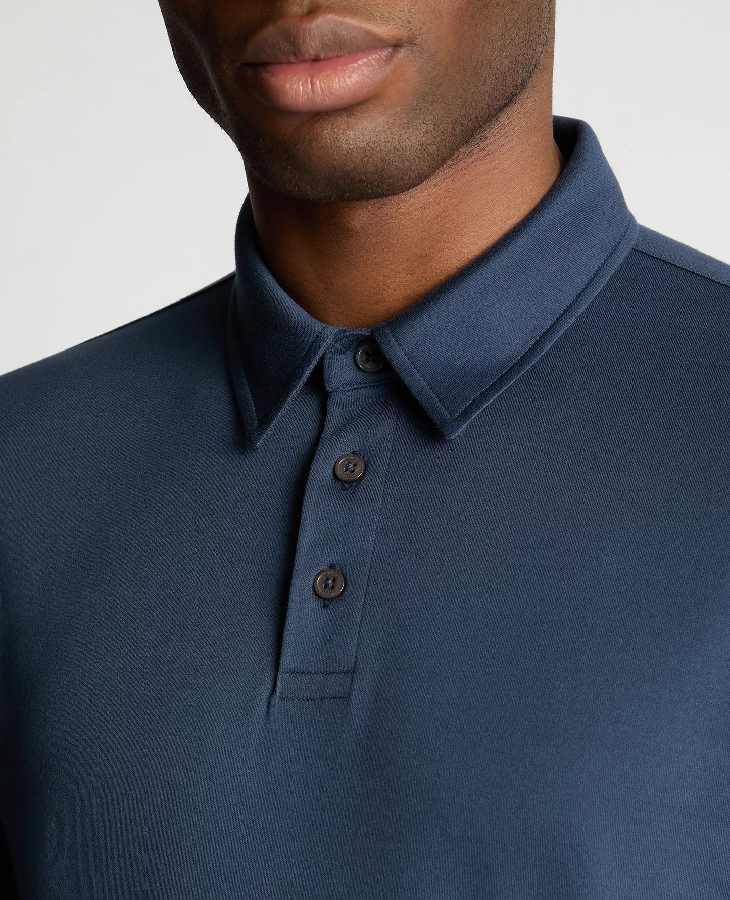 Close-up of a person wearing a blue polo shirt with a plain background