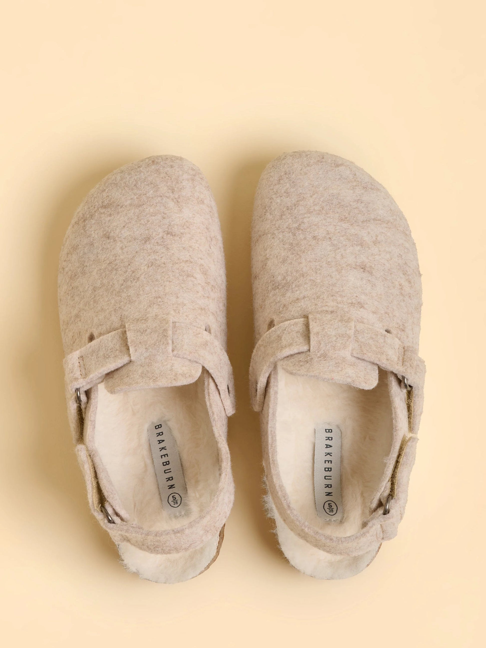 Pair of beige shoes with a strap on a beige background