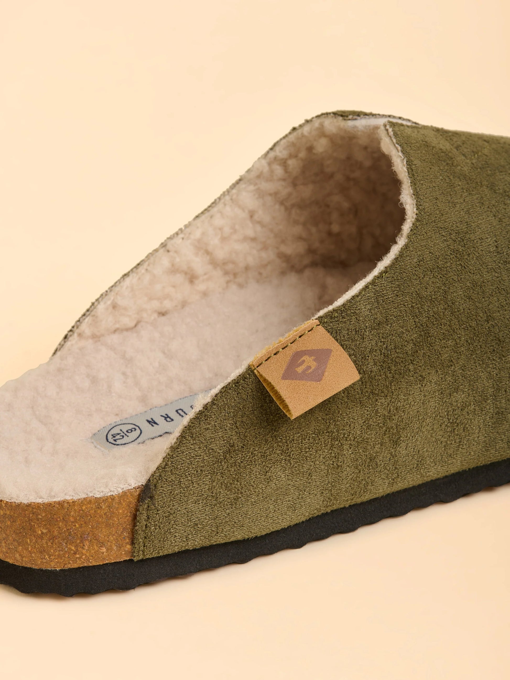 Green slipper with brown interior and visible brand label on a beige background