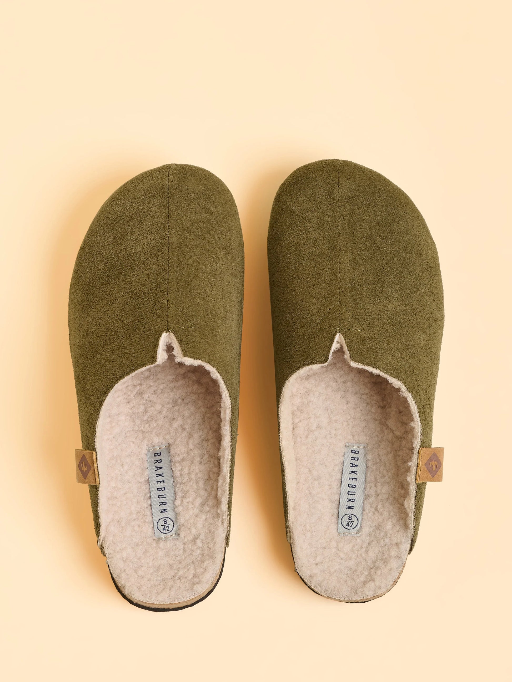 Pair of green slippers with beige soles on a beige background
