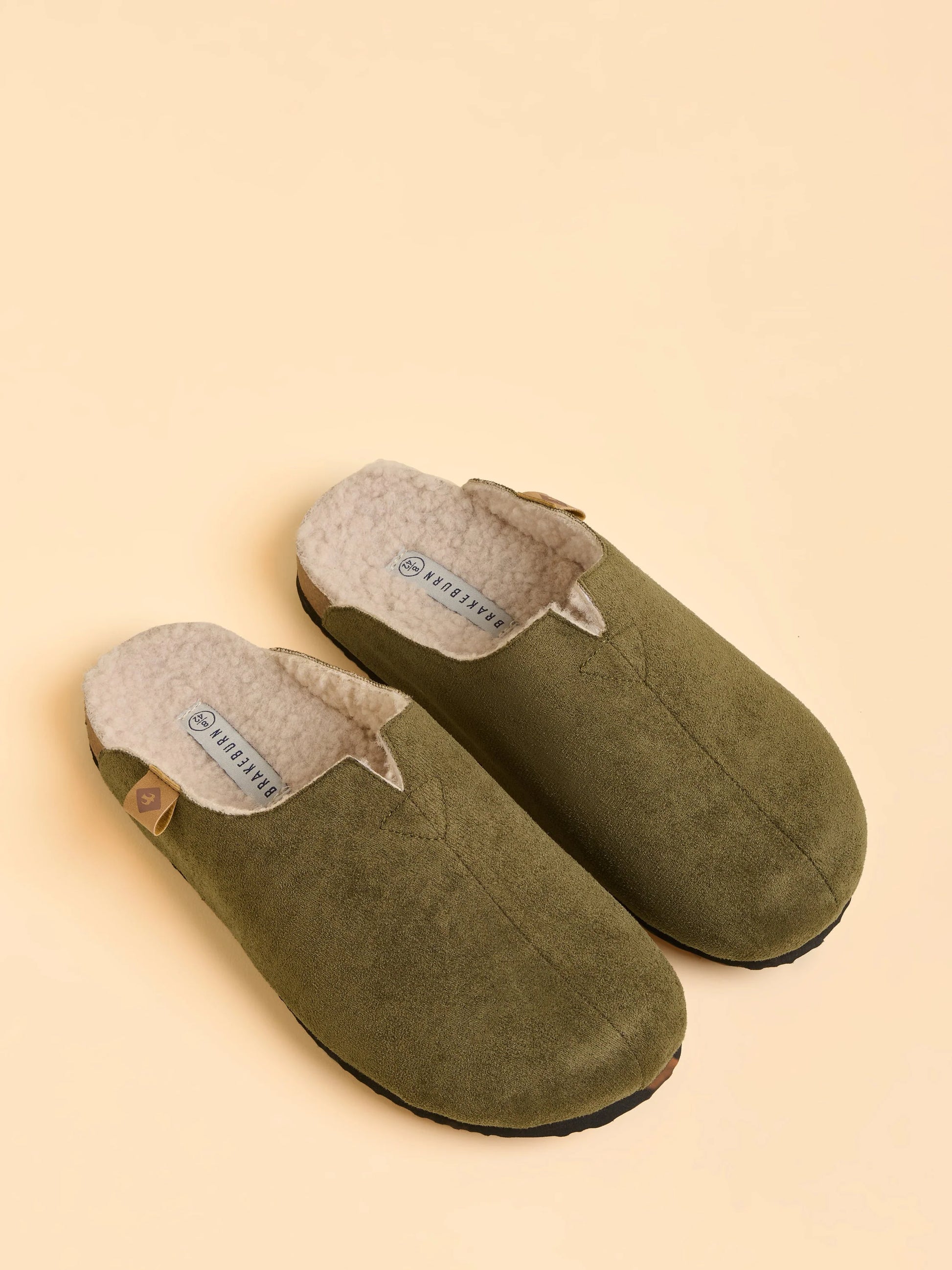 Pair of green slippers with gray interior on a beige background