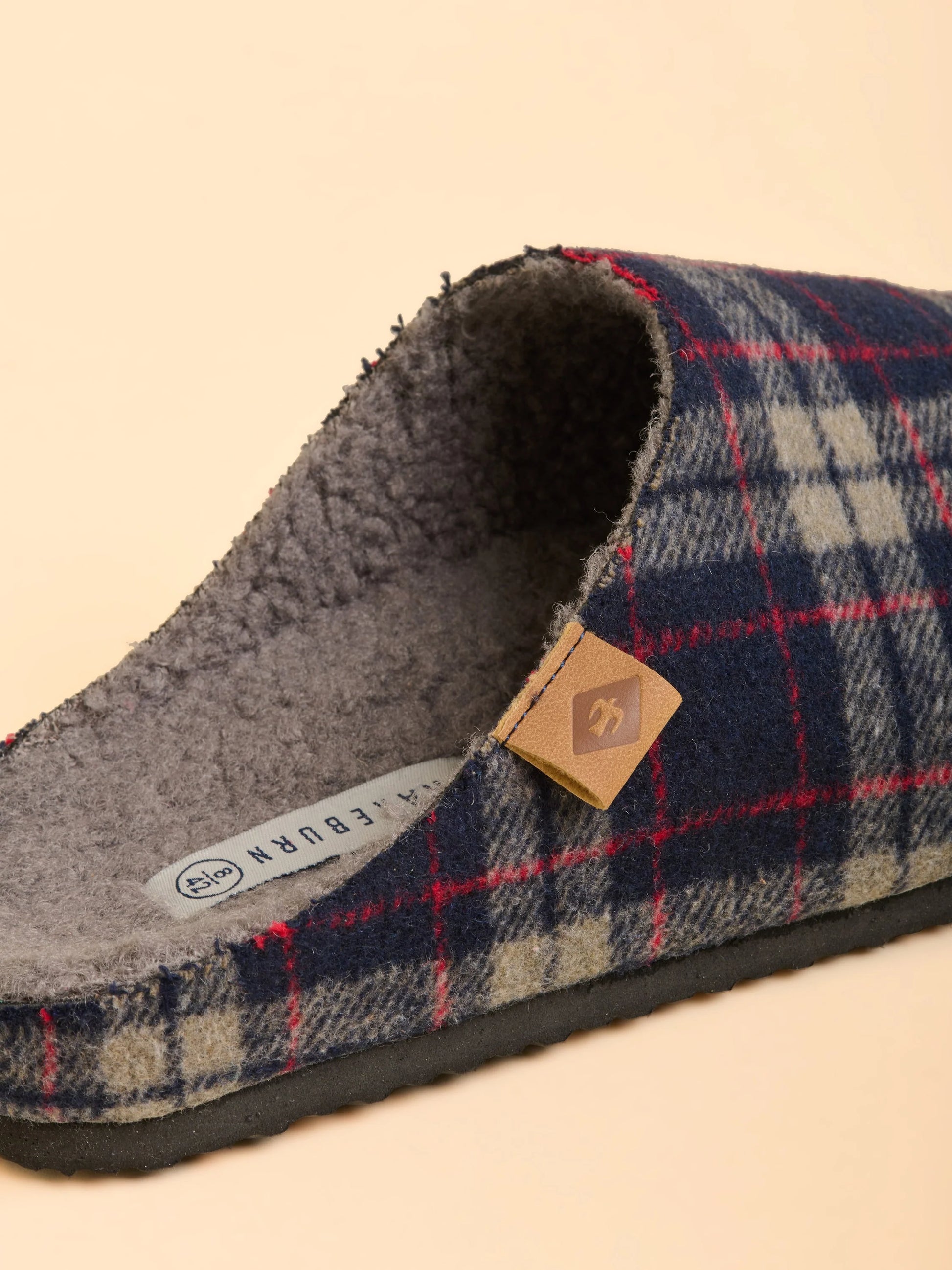 Plaid slipper with a visible brand tag on a beige background