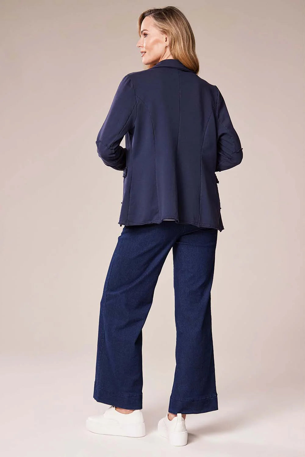 Woman wearing a navy blue outfit with a matching jacket and pants on a beige background