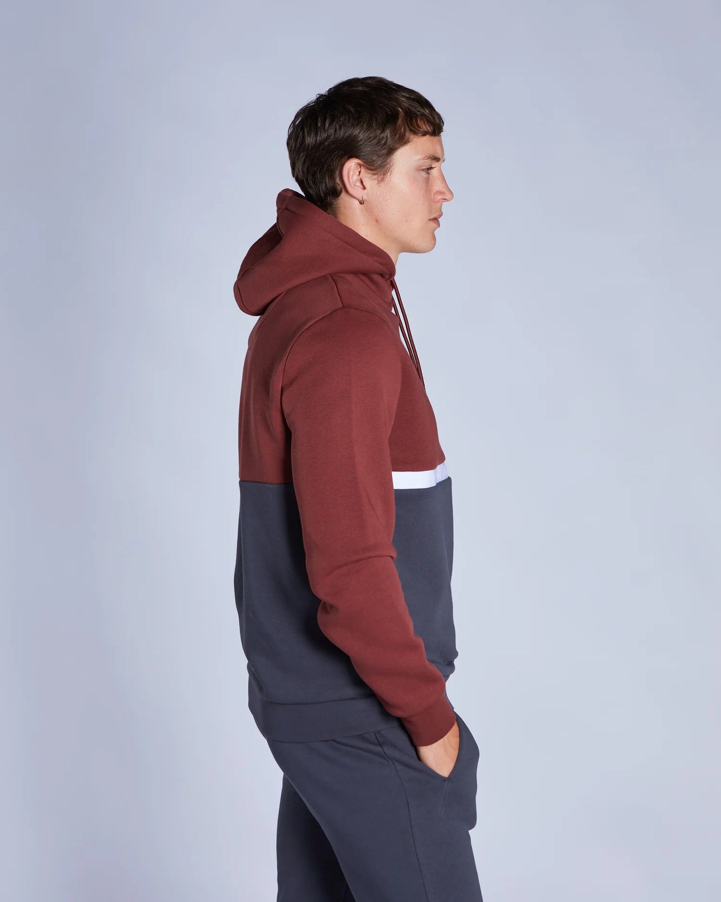 Person wearing a two-tone hoodie with maroon and gray sections on a light gray background