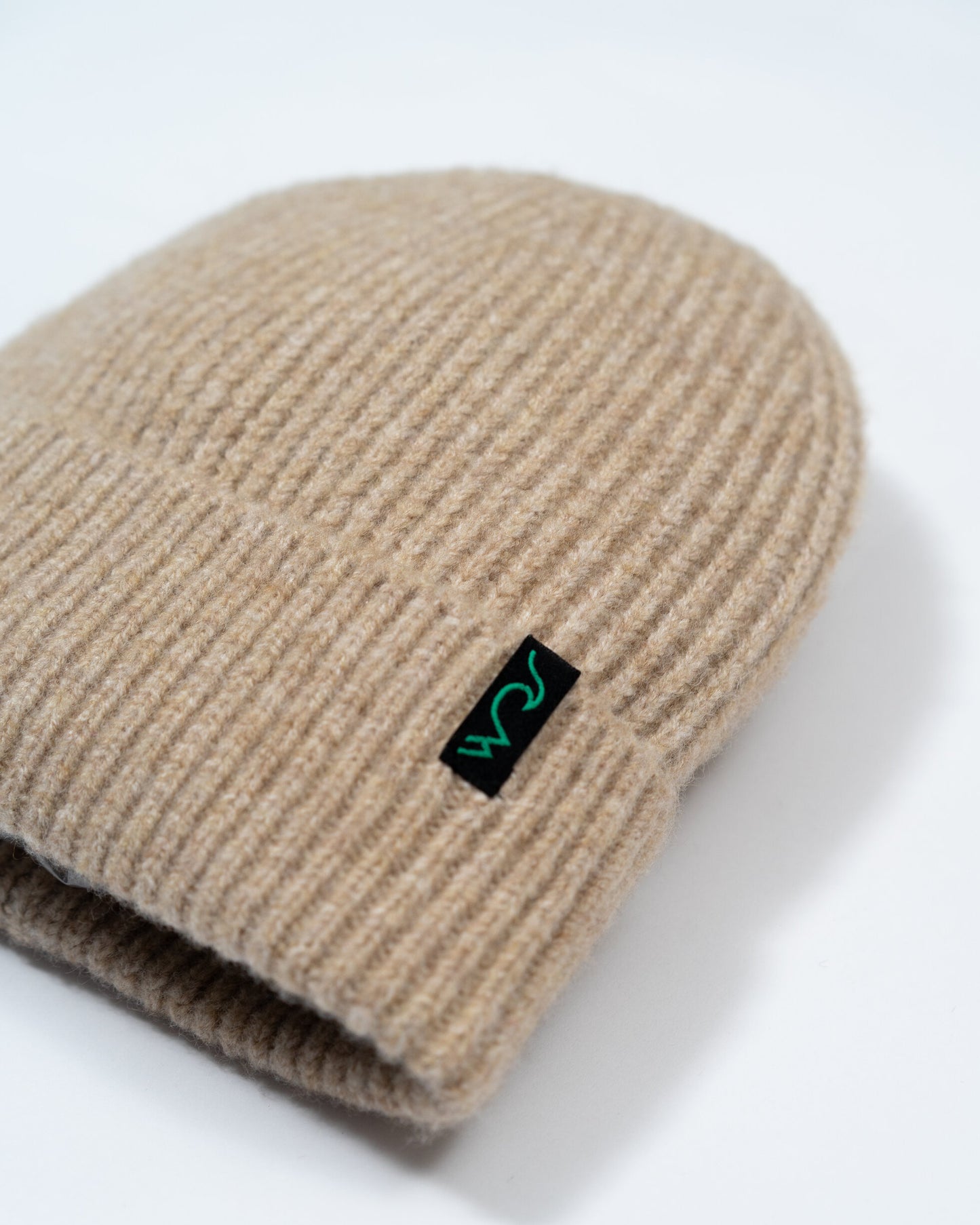 Beige knit beanie with a black and green logo on a white background