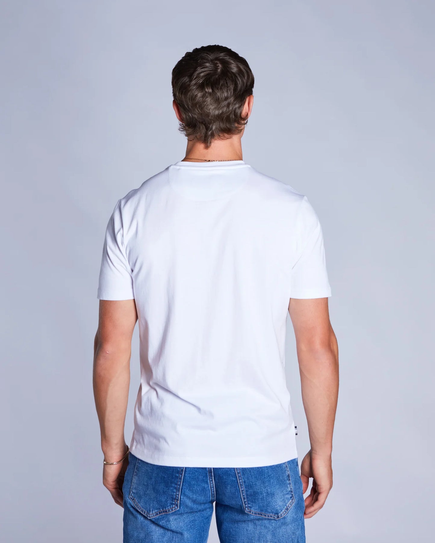 Man wearing a plain white t-shirt and blue jeans against a light gray background