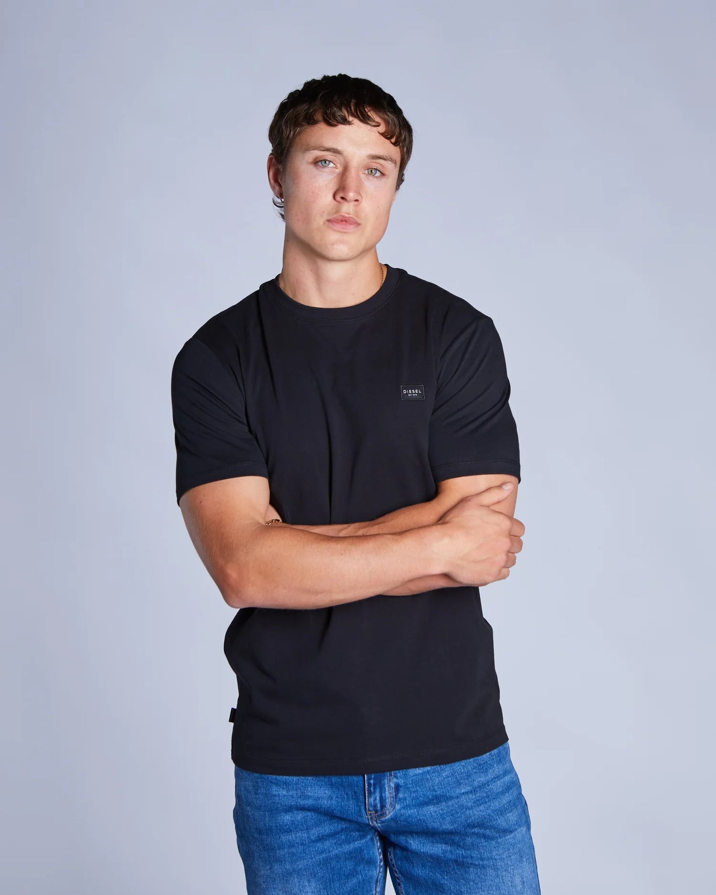 Man wearing a black t-shirt and blue jeans against a gray background