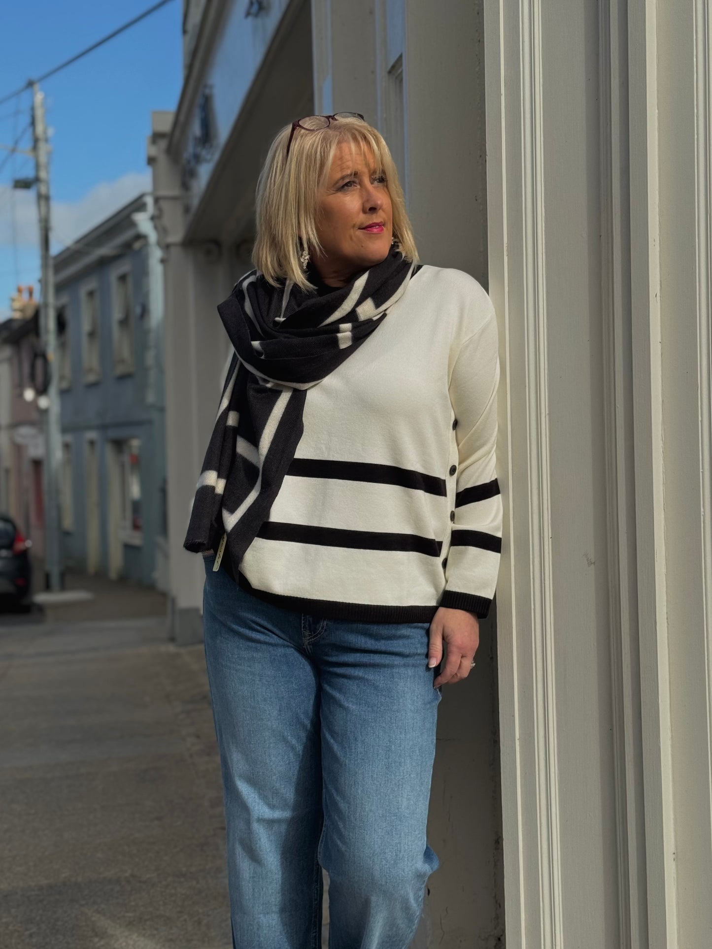 Woman wearing a striped sweater and scarf standing on a street corner.