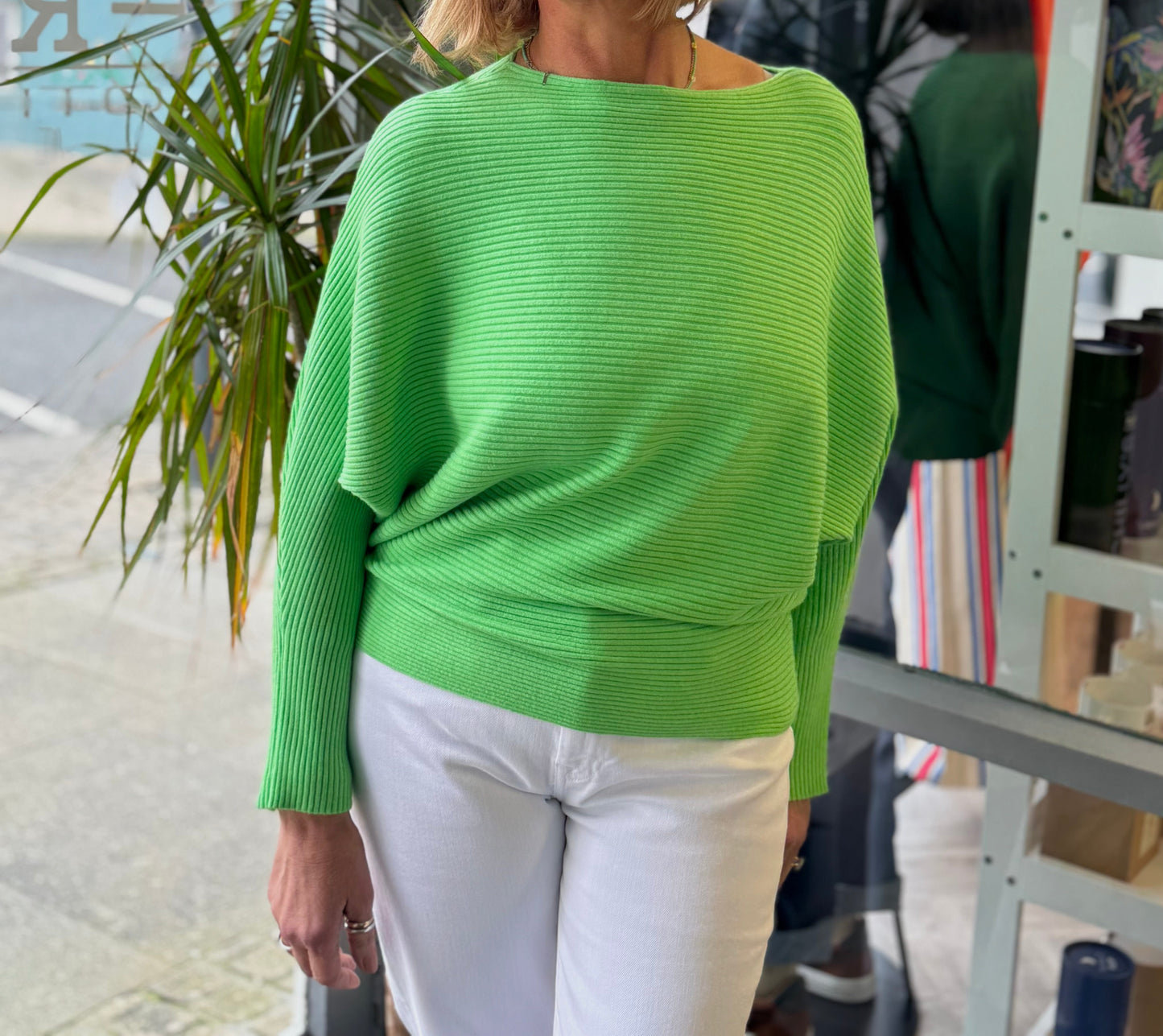 Woman wearing a bright green sweater and white pants standing in front of a store window.