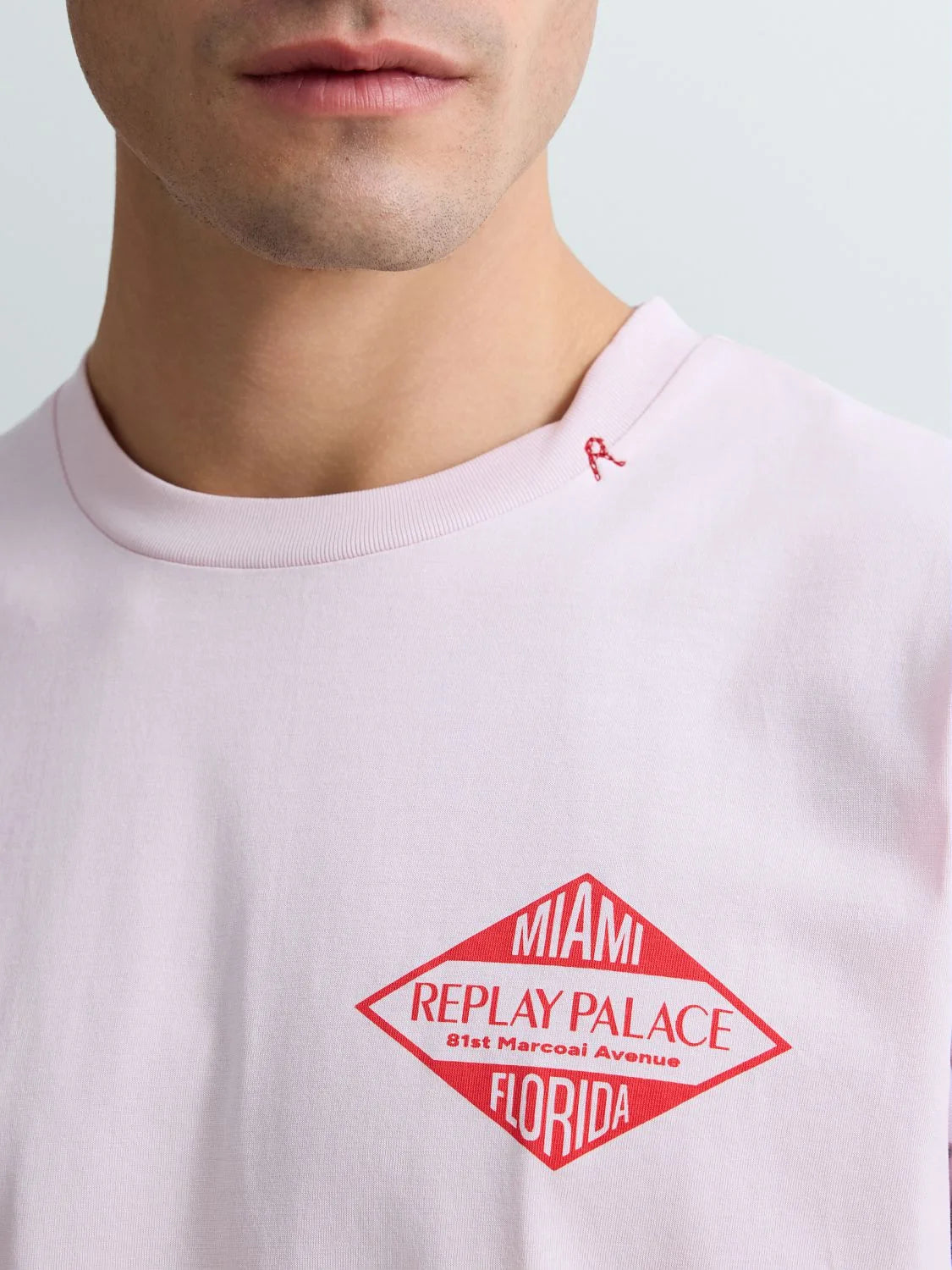 Close-up of a light pink t-shirt with a red logo and text on a white background