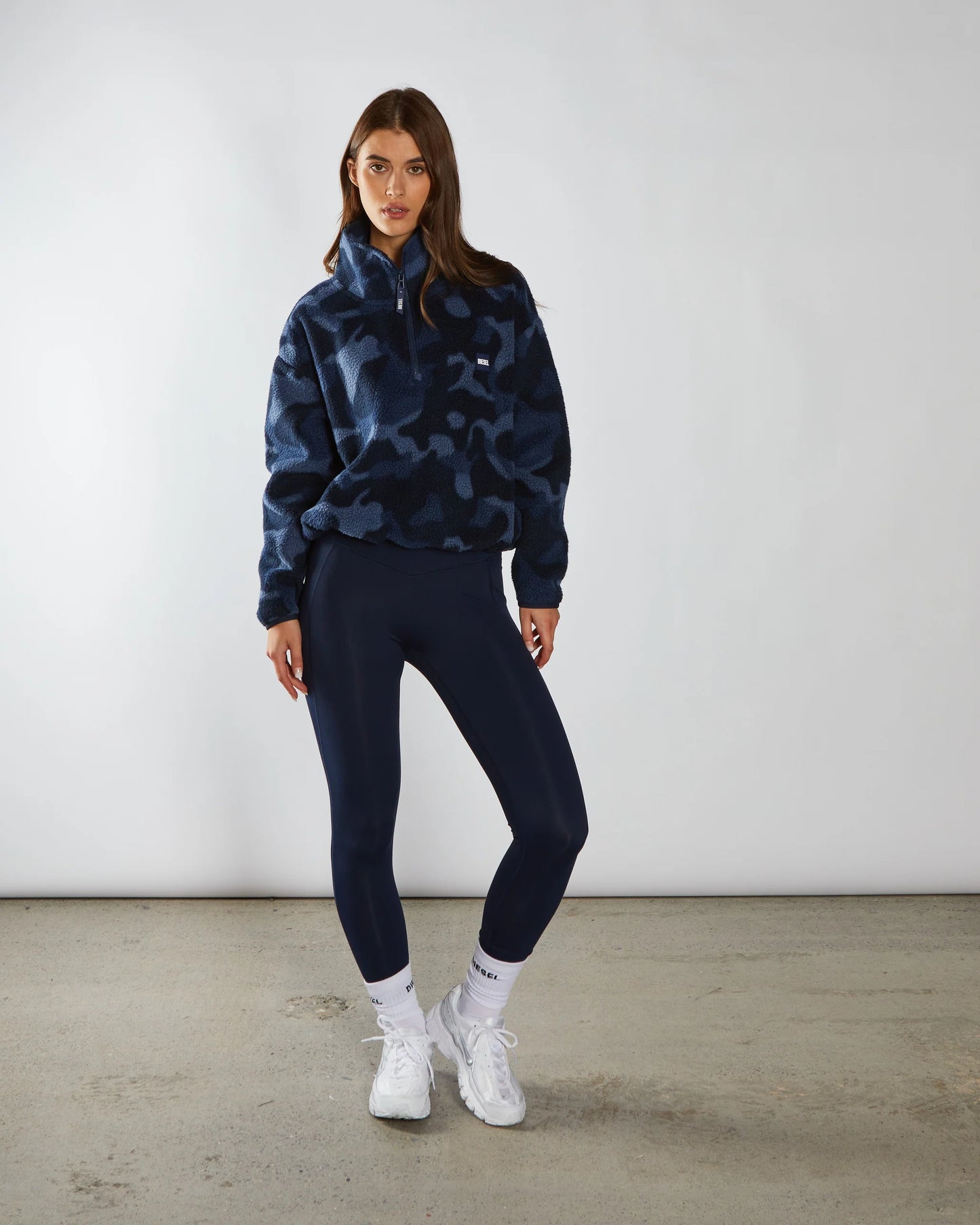 Person wearing a blue camouflage hoodie and black leggings with white sneakers on a plain background