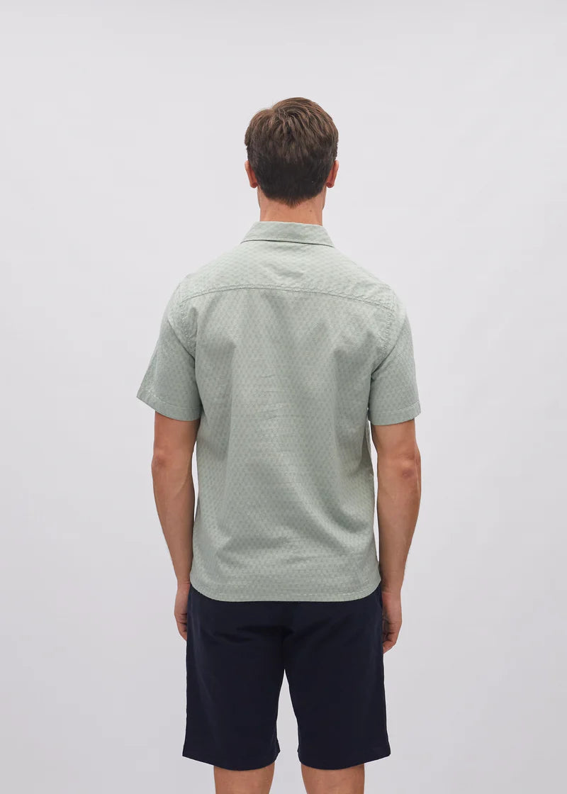 Man wearing a green patterned shirt and navy shorts on a white background