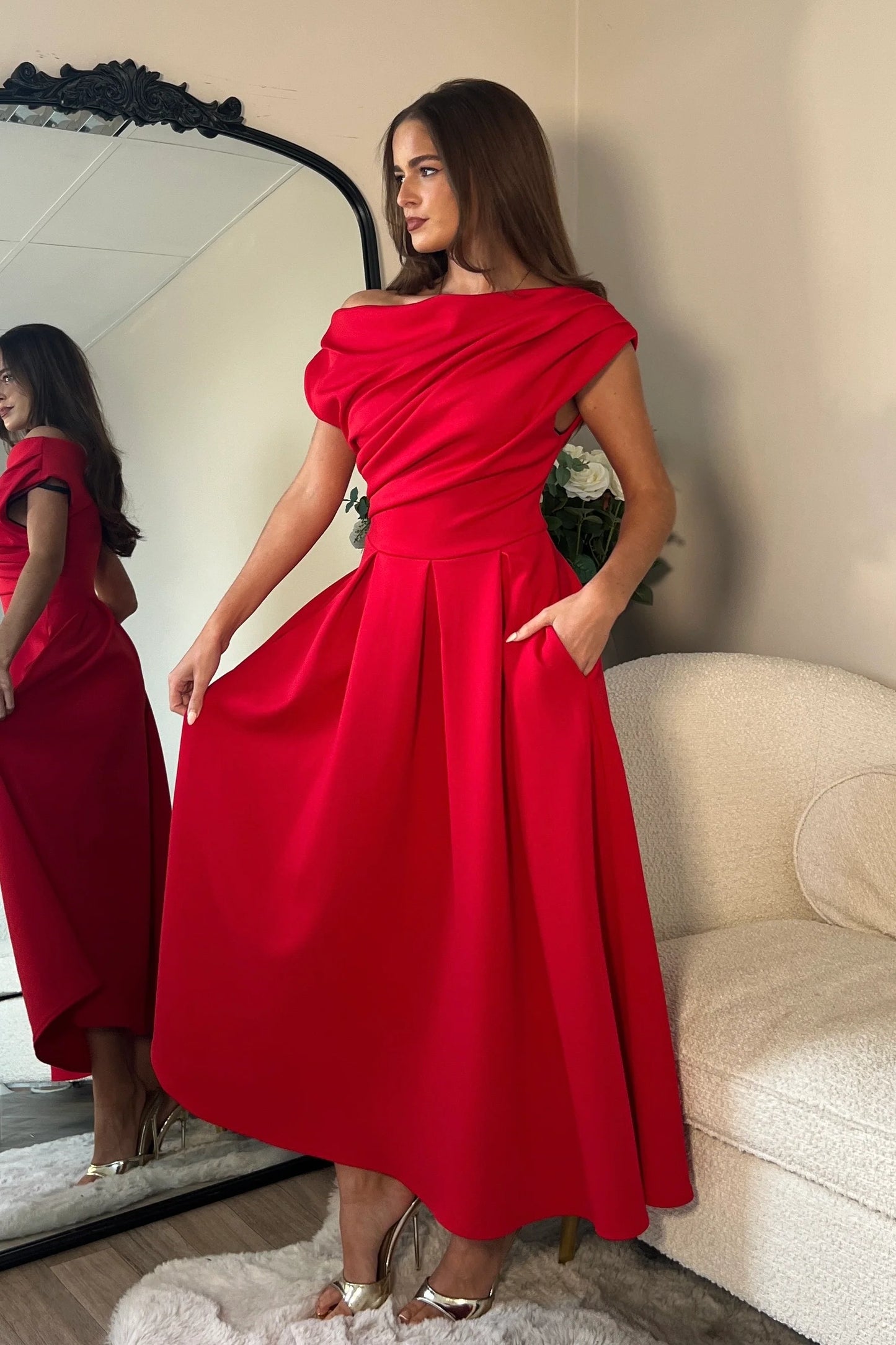 Woman in a red off-shoulder dress standing in front of a mirror.