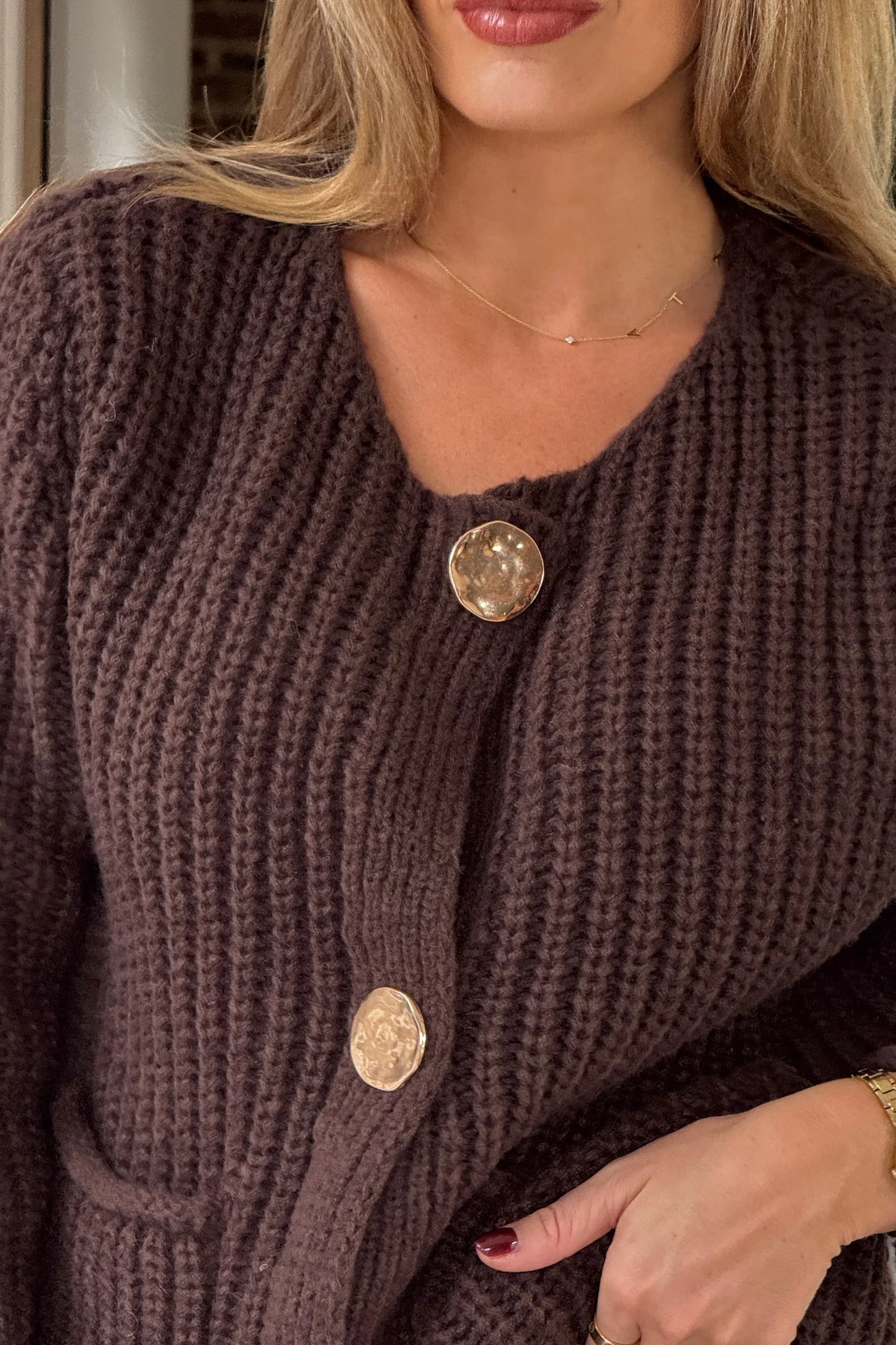 Close-up of a person wearing a brown knitted cardigan with gold buttons.