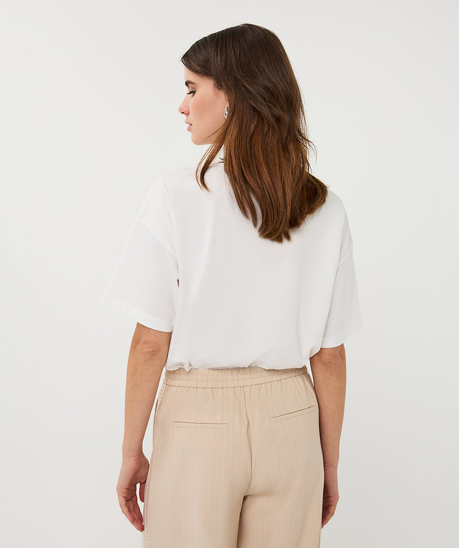Woman wearing a white blouse and beige pants against a plain background