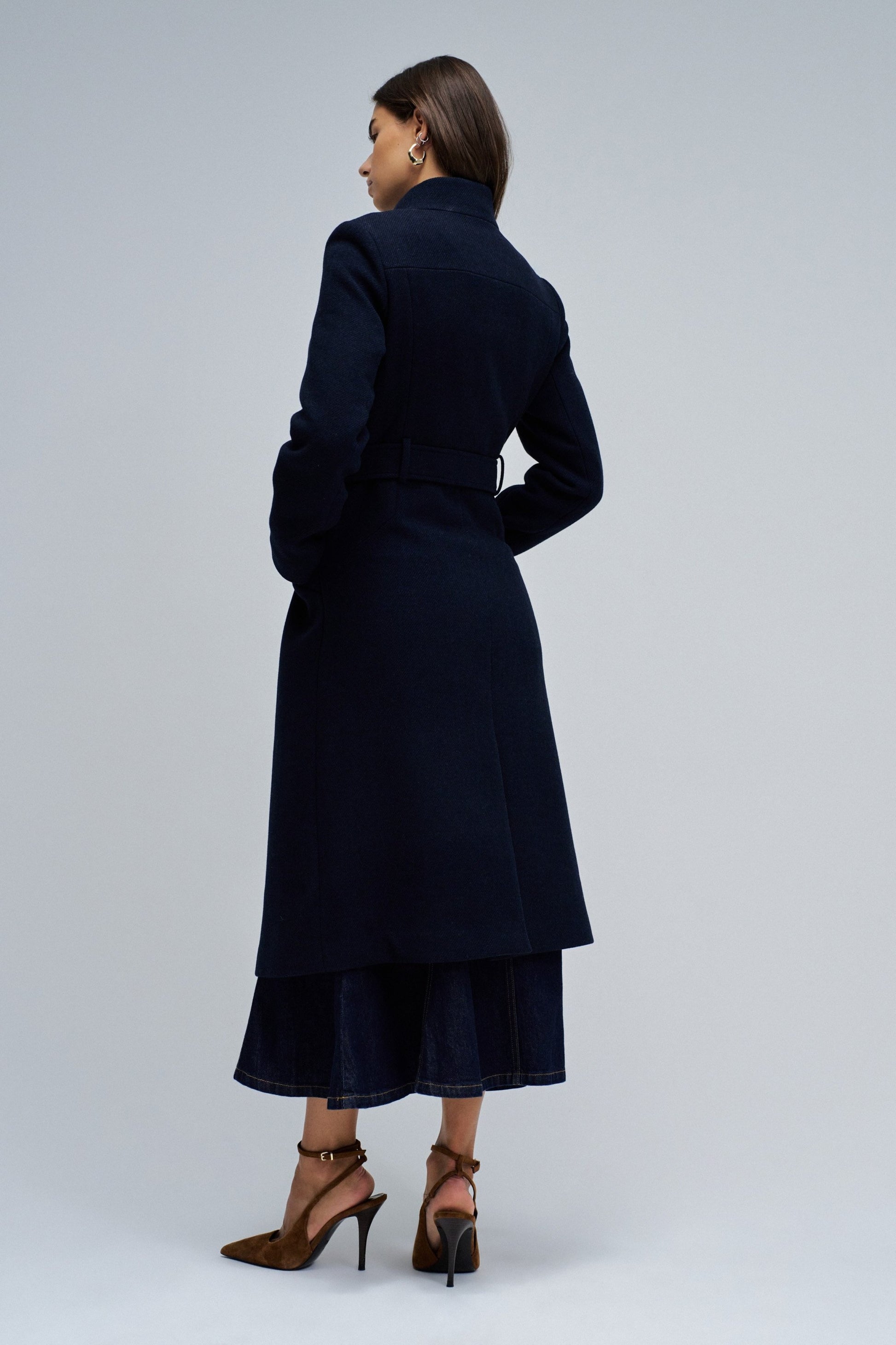 Woman wearing a long navy coat on a plain background