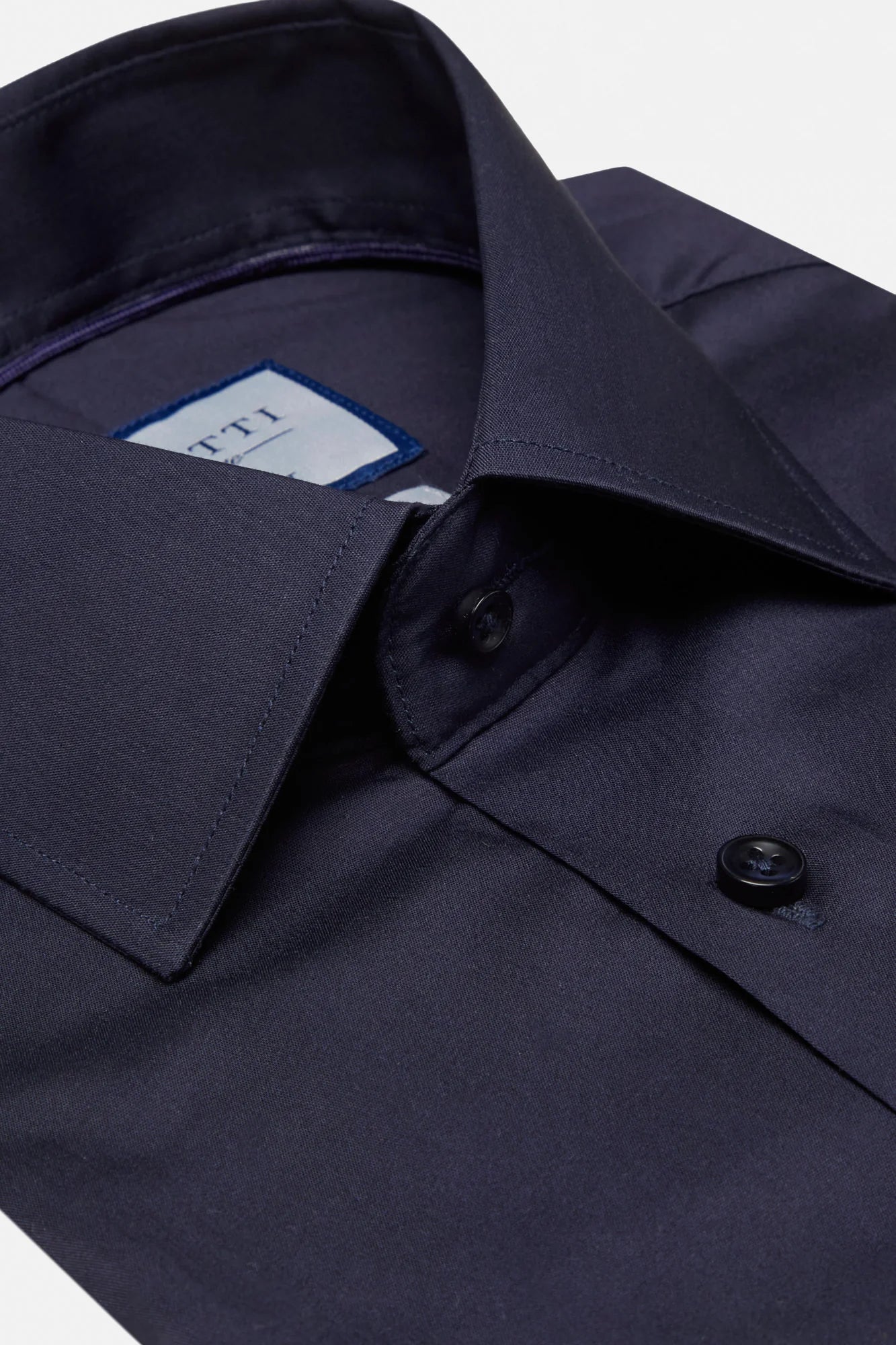 Close-up of a navy blue dress shirt with a button and collar detail.