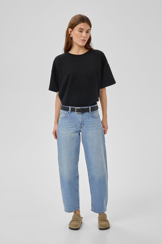Women wearing black tee with light wash barrel jeans with taupe loafers on a white background