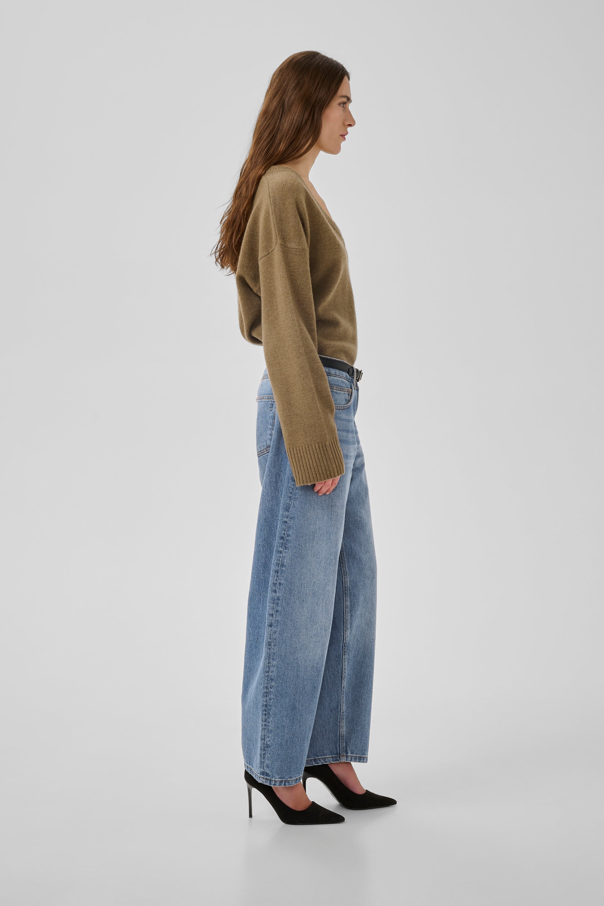 Woman wearing a green sweater and light blue jeans on a white background