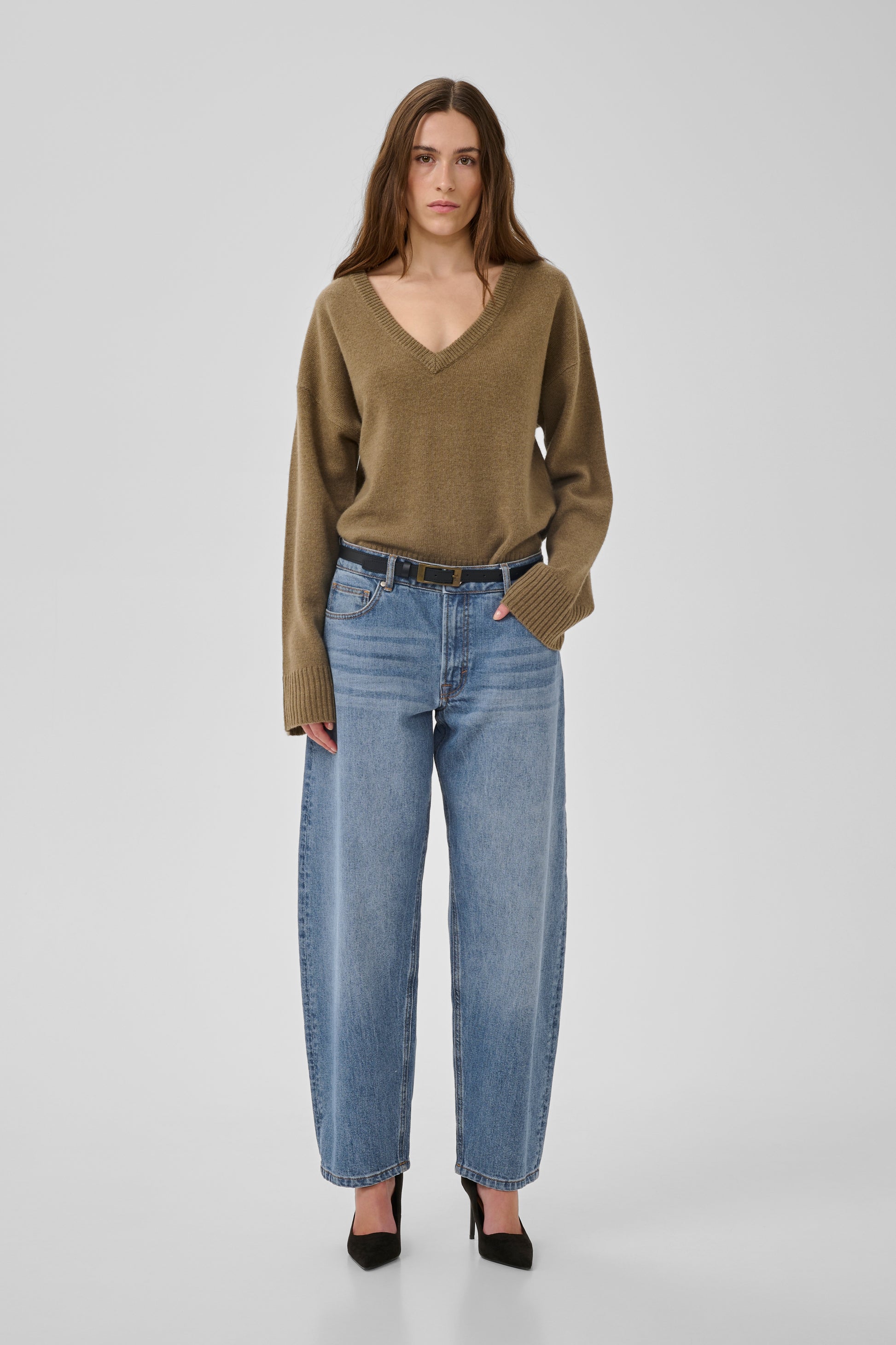 Woman wearing a green sweater and blue jeans on a white background