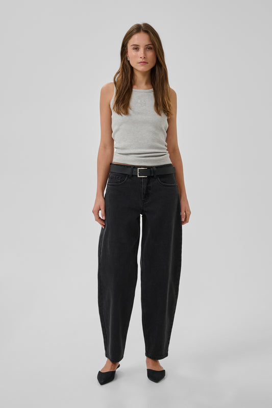 Woman wearing a white tank top and black pants on a light gray background