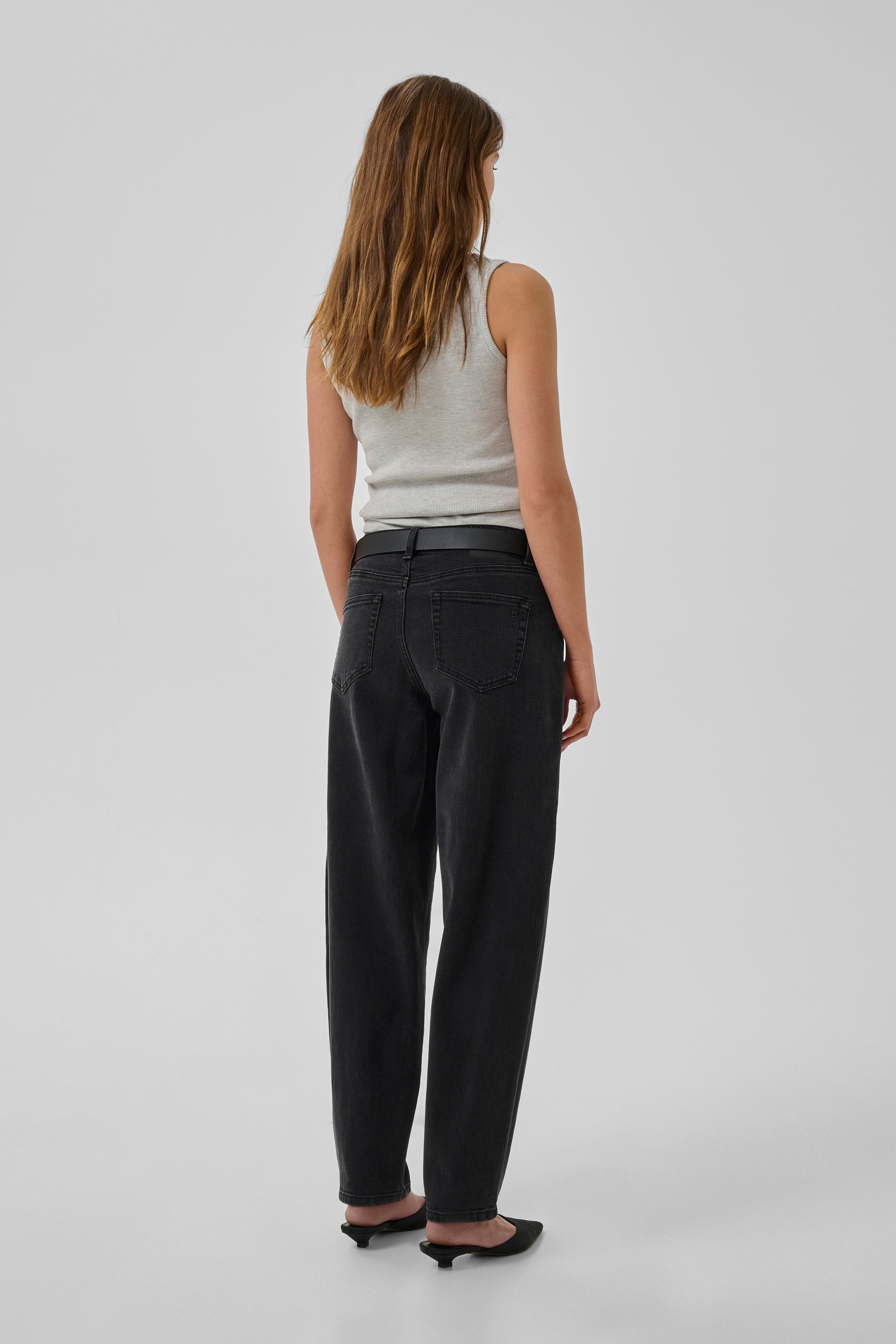 Woman wearing black pants and a white top on a plain background
