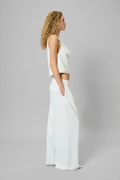 Woman wearing a white sleeveless top and wide-leg pants on a gray background