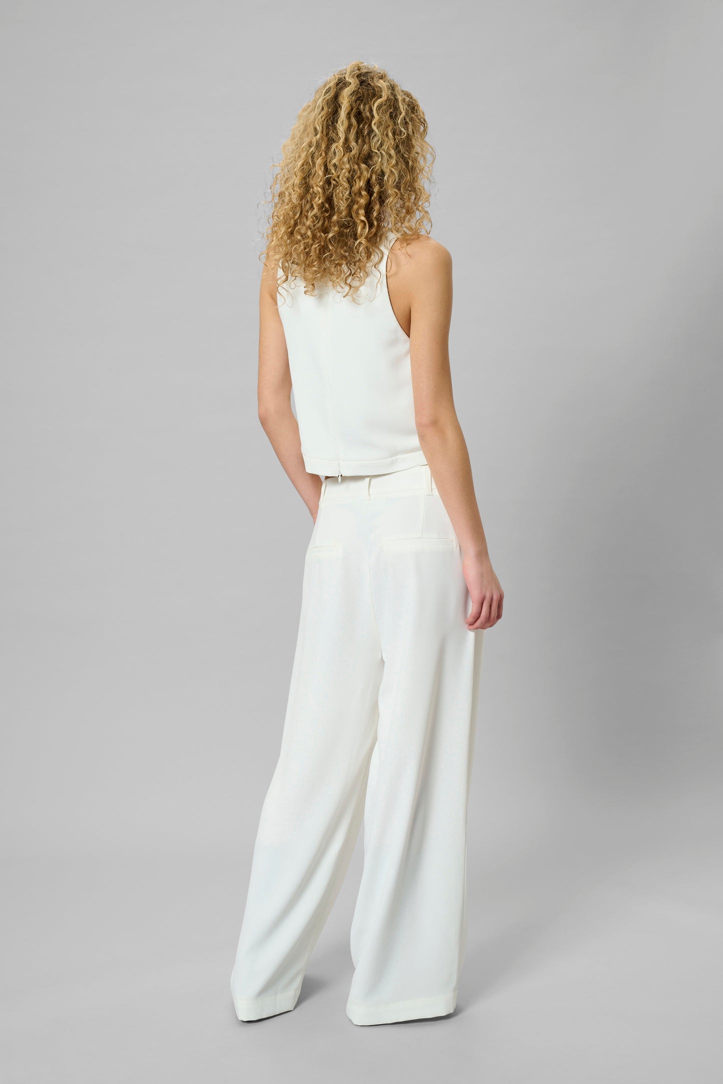 Woman wearing a white sleeveless top and wide-leg pants on a gray background