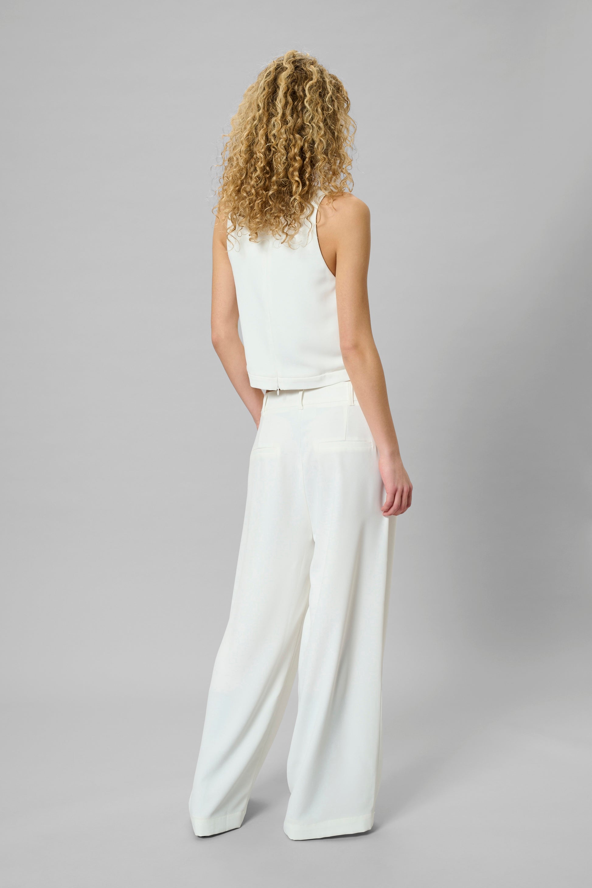 Woman wearing a white sleeveless top and wide-leg pants on a gray background