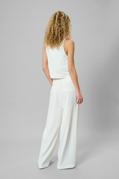 Woman wearing a white sleeveless top and wide-leg pants on a gray background