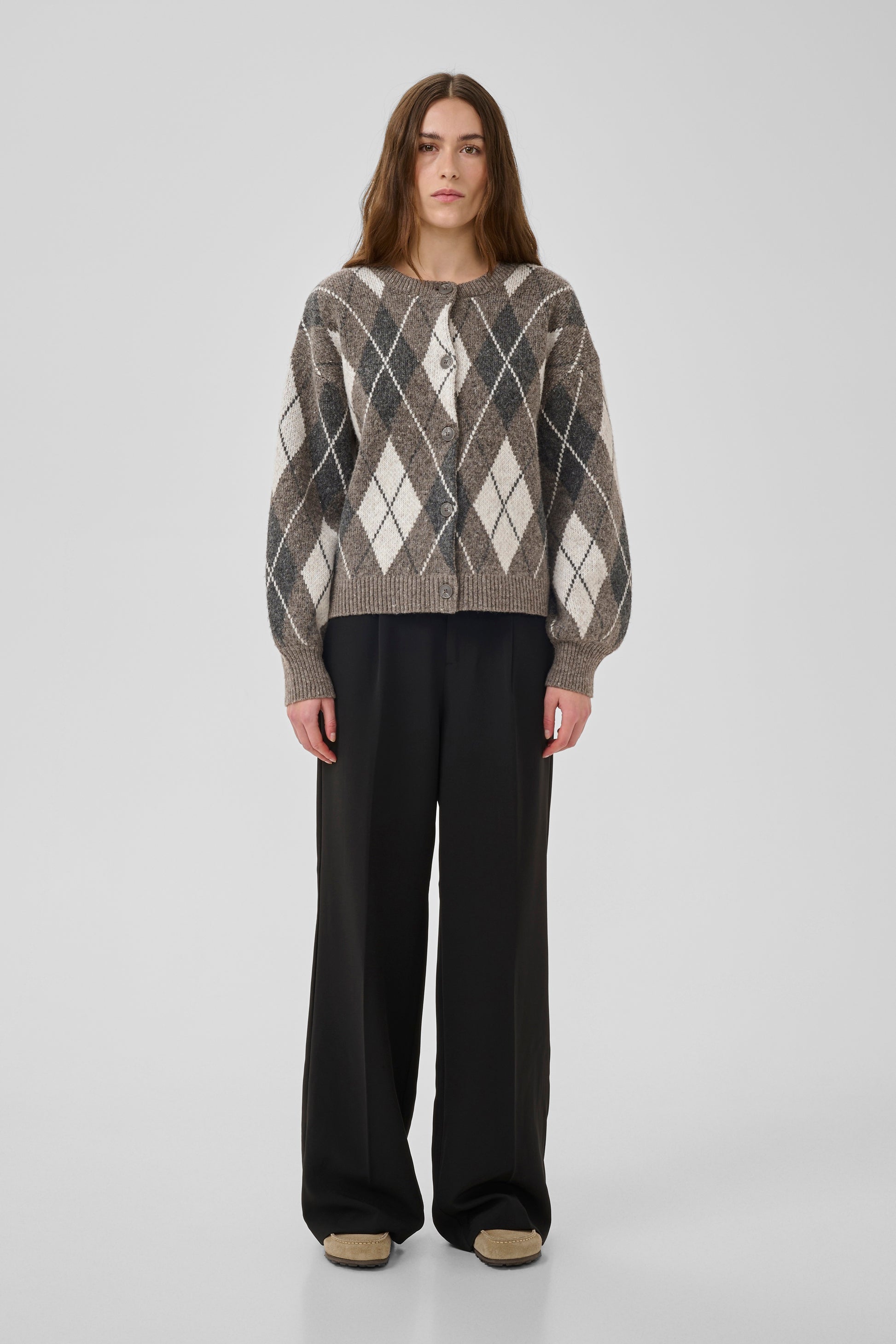 Person wearing a patterned sweater and black pants on a white background