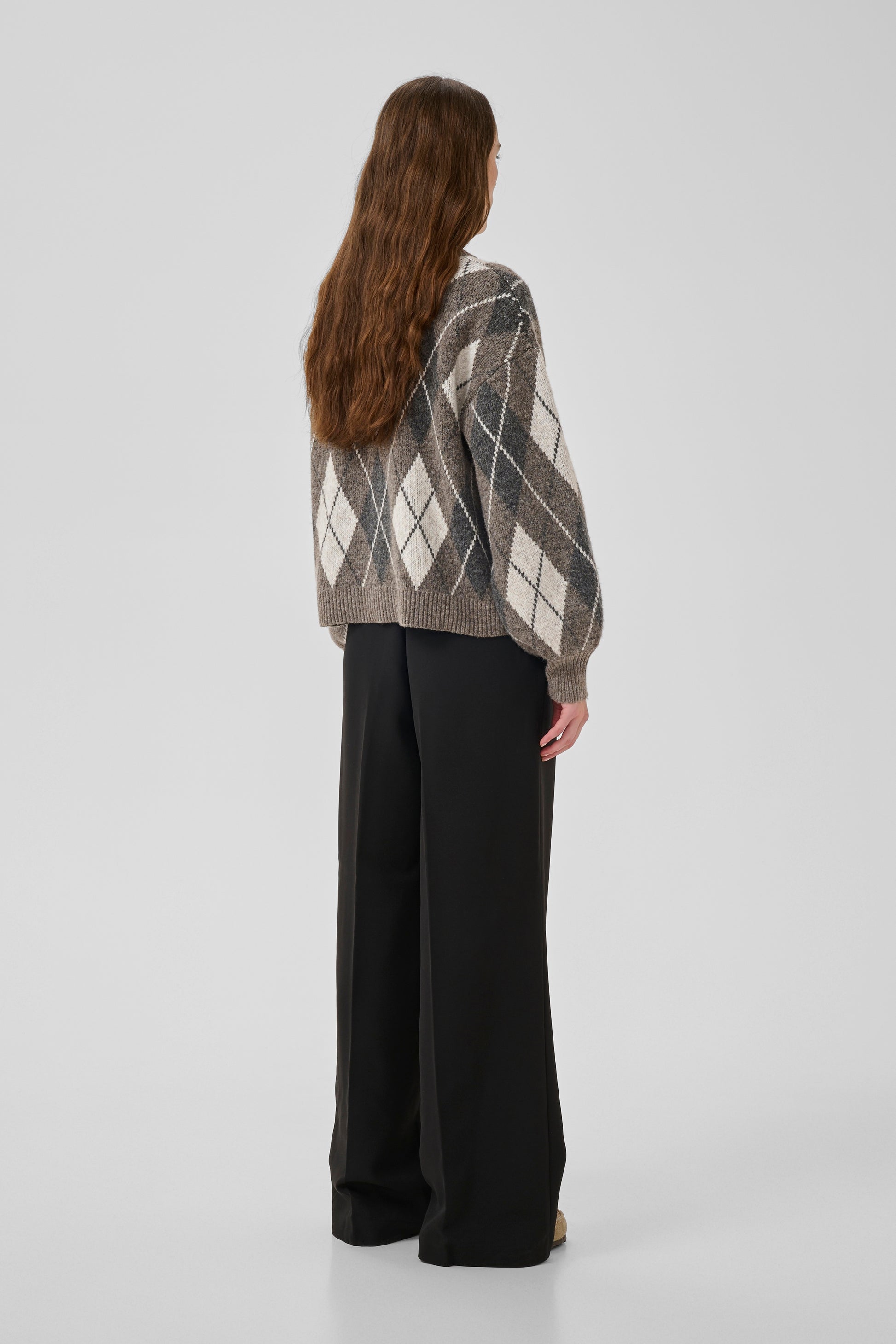 Woman wearing a patterned sweater and black pants on a white background
